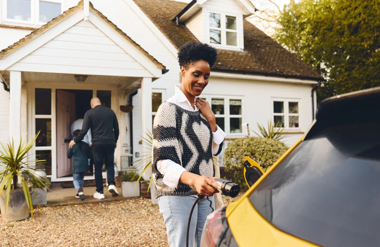Woman plugging in electric car charger into her yellow hatchback outside of her house