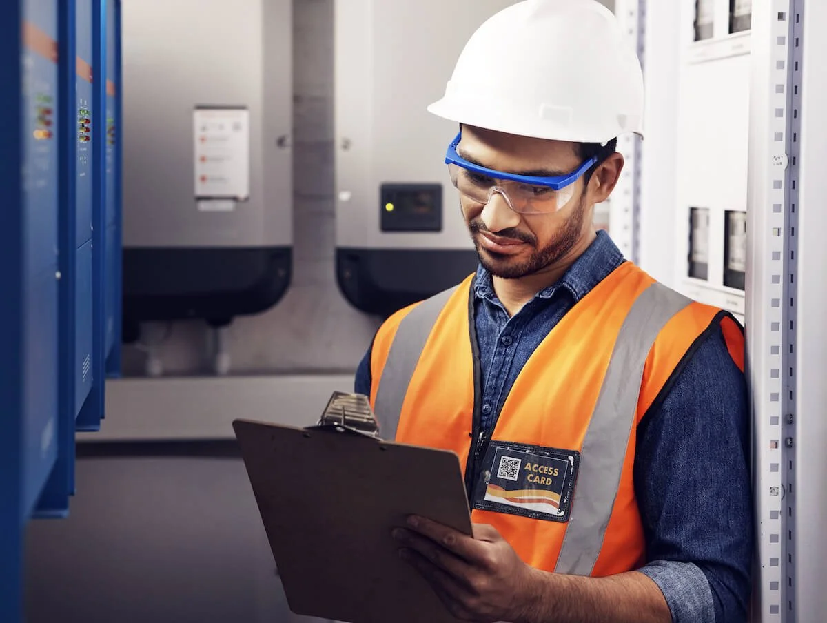 electrician technician in control room, writing notes and machine maintenance on clipboard.