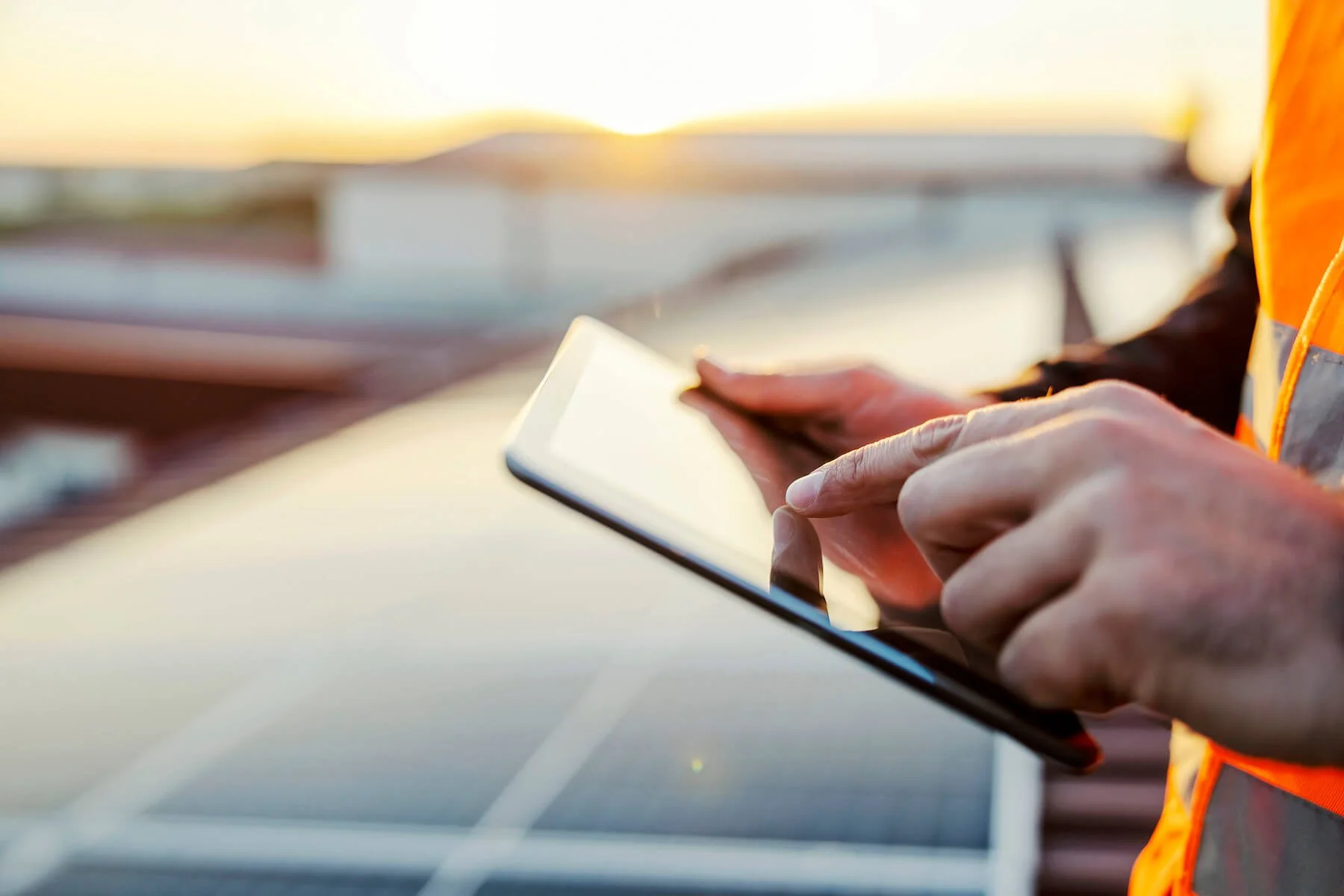 Electrical engineer holding a tablet standing next to solar panels on a roof of a commercial building