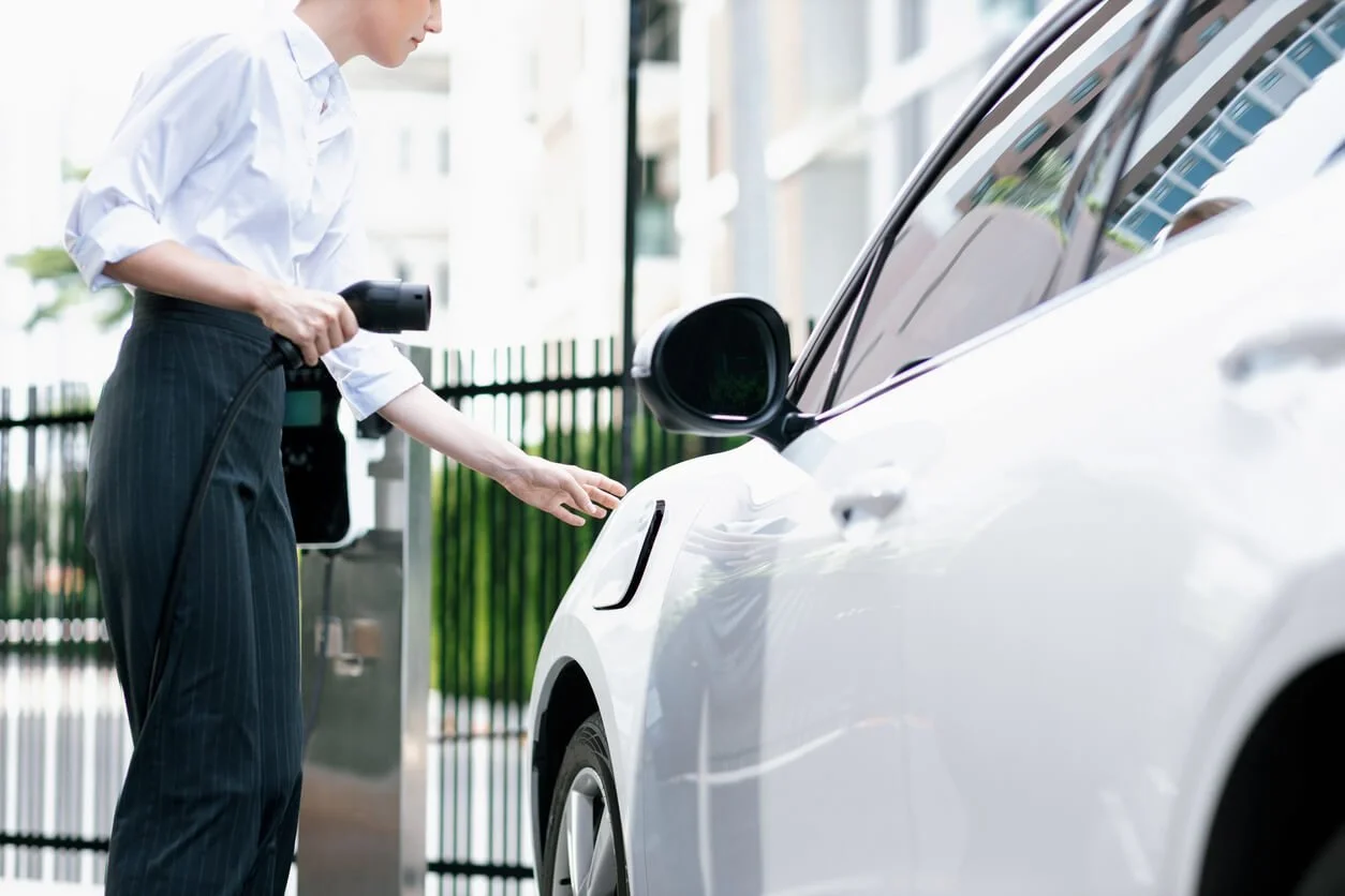 woman plugging an EV charger into her car in the parking lot at a multi-unit dwelling