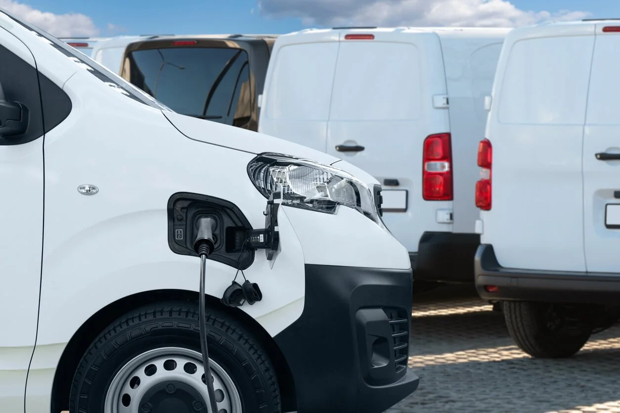 Commercial fleet of white vans plugged into EV chargers