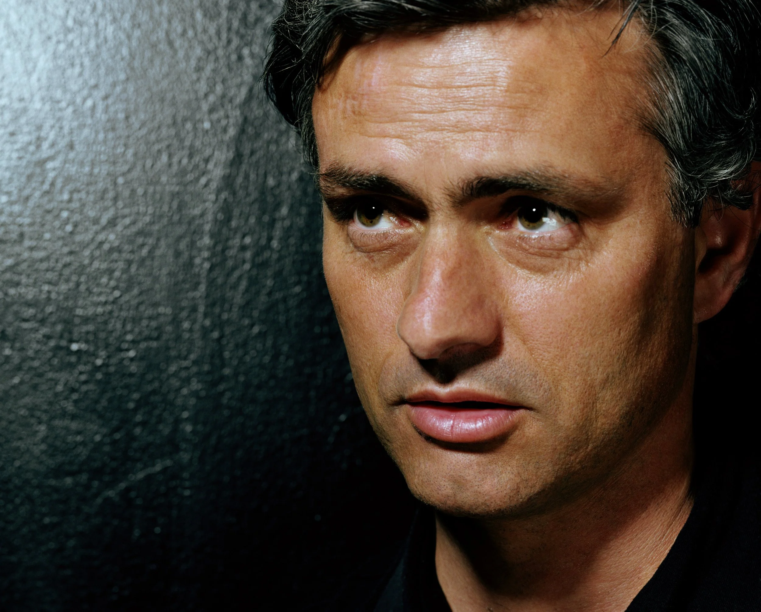 Close-up of a man's face, showing his forehead, eyes, and part of his nose and lips. He has dark hair, light skin, brown eyes, and appears to be looking slightly to the side. The background is a textured gray surface.