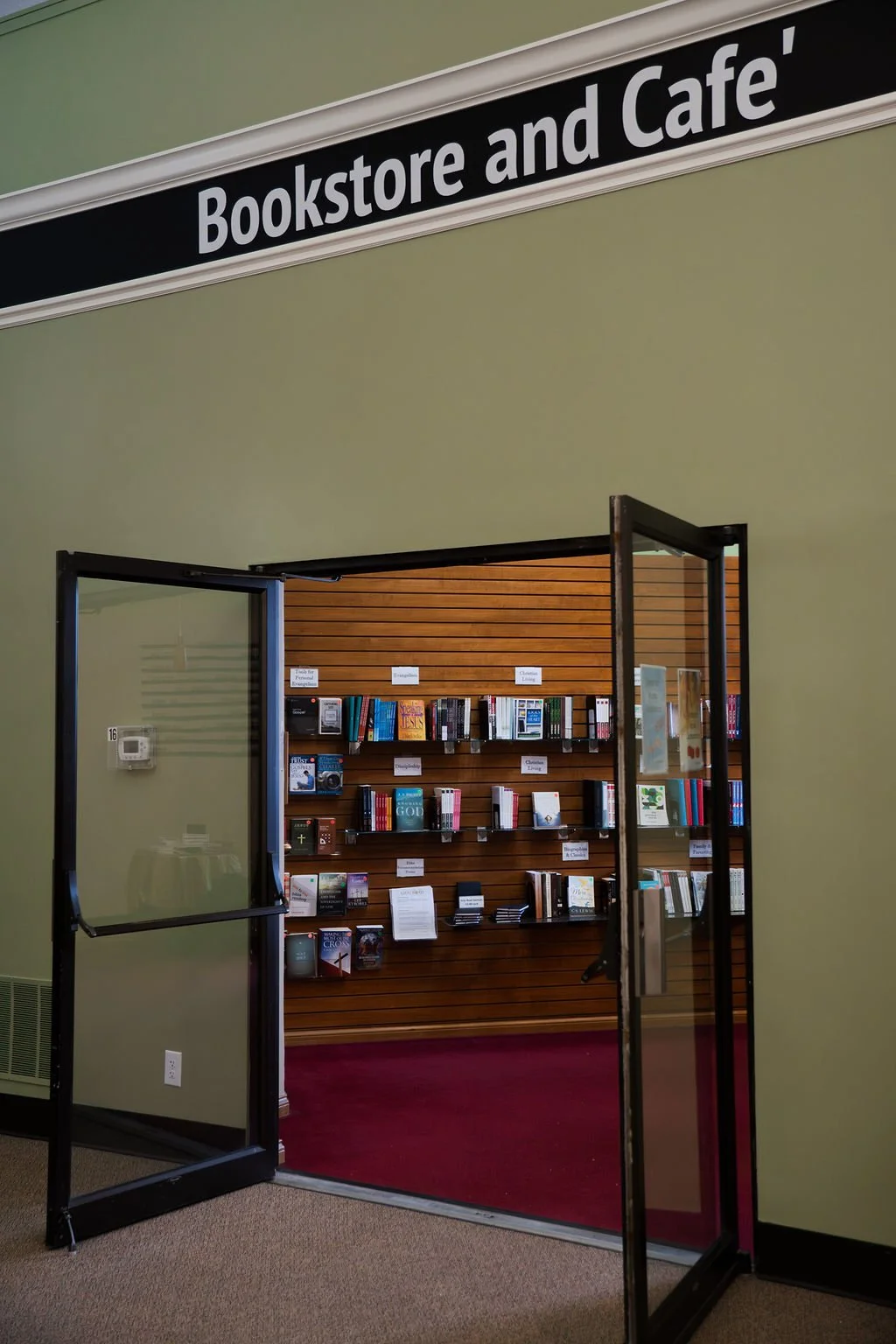 Entrance to a bookstore and café with books displayed on wooden shelves visible through an open glass door.