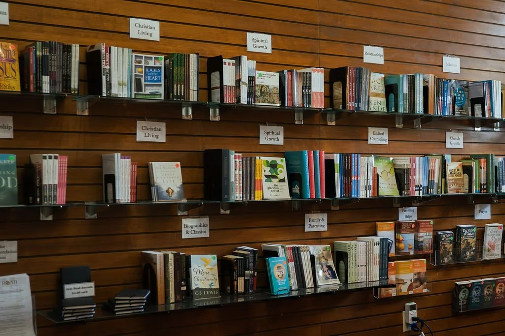 Bookshelves filled with various books in a library, organized by categories such as Christian Living, Spiritual Growth, Relationships, Biblical Counseling, Church Growth, Biographies & Classics, Family & Parenting, Parenting Help, and Prayer.