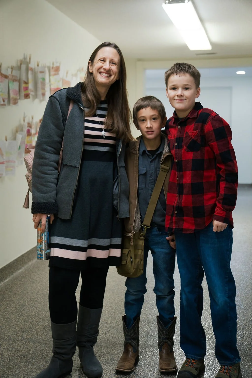 A woman and two boys standing together indoors, smiling for the camera.