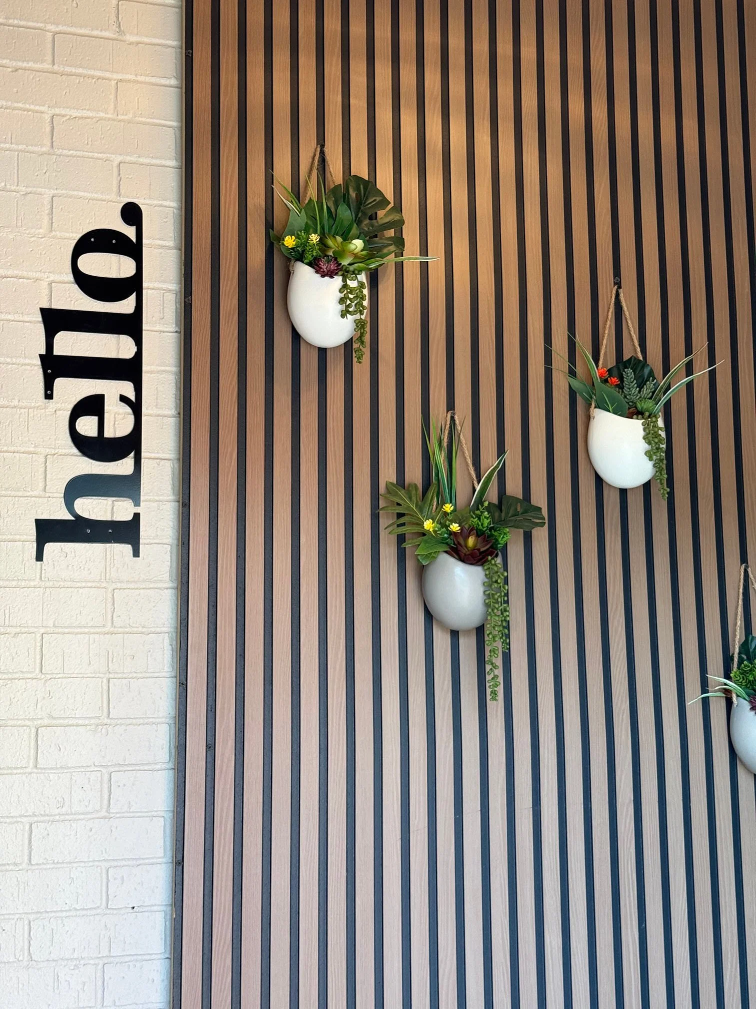 Arched view of modern restaurant decor featuring a wood slat wall, hanging planters, and a welcoming hello sign at U&I Korean Fusion in Murfreesboro, TN.