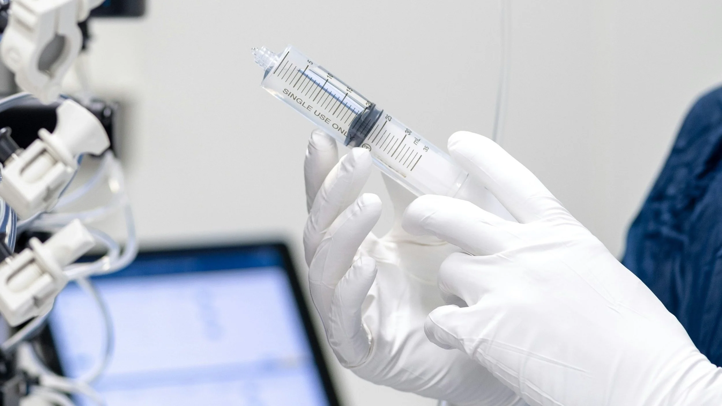 A gloved hand holding a large syringe in a medical setting.