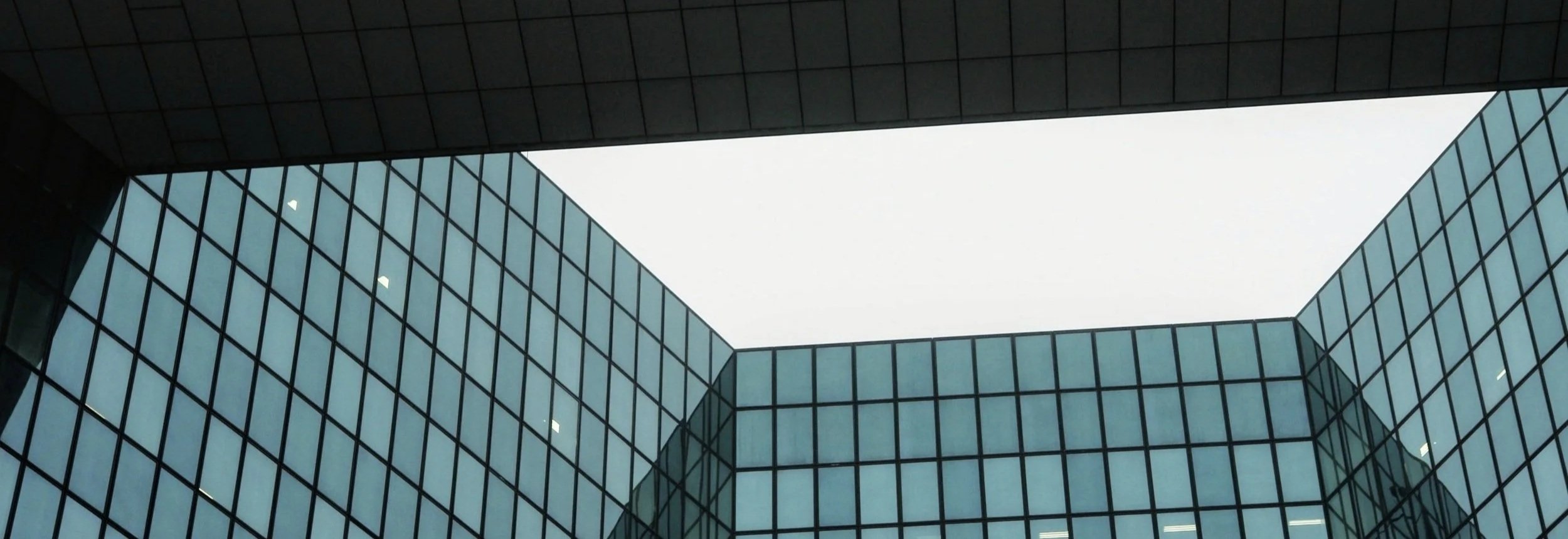Low-angle view of modern glass office building with a rectangular opening in the roof, showing a cloudy sky.