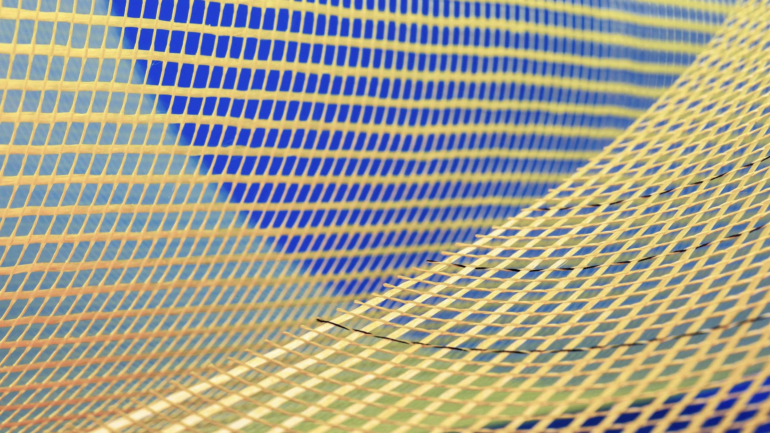 Close-up view of yellow plastic mesh fencing with a blue mesh background, curved and overlapping.