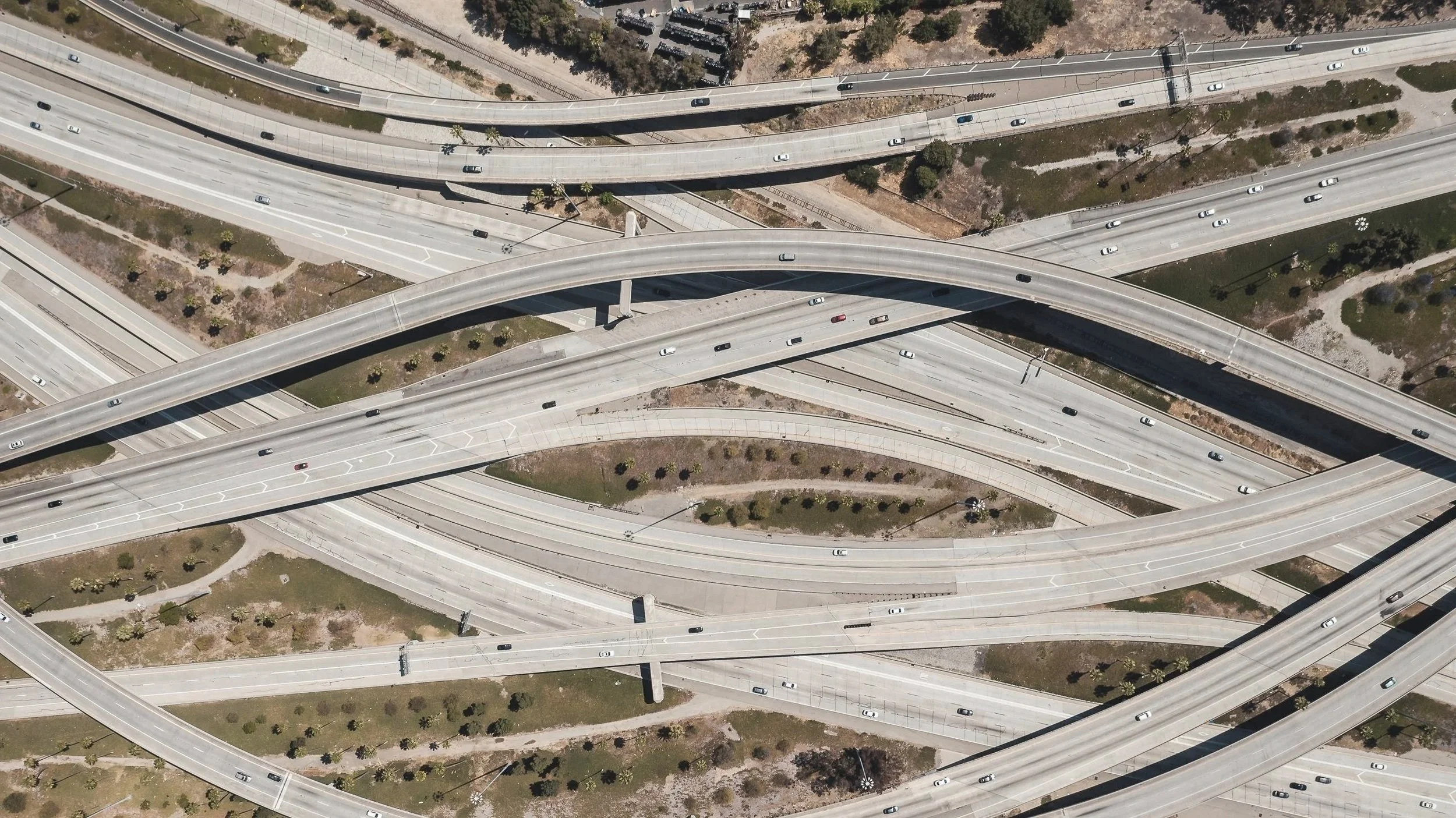 Aerial view of a complex highway interchange with multiple overpasses, ramps, and roads with cars traveling in different directions.
