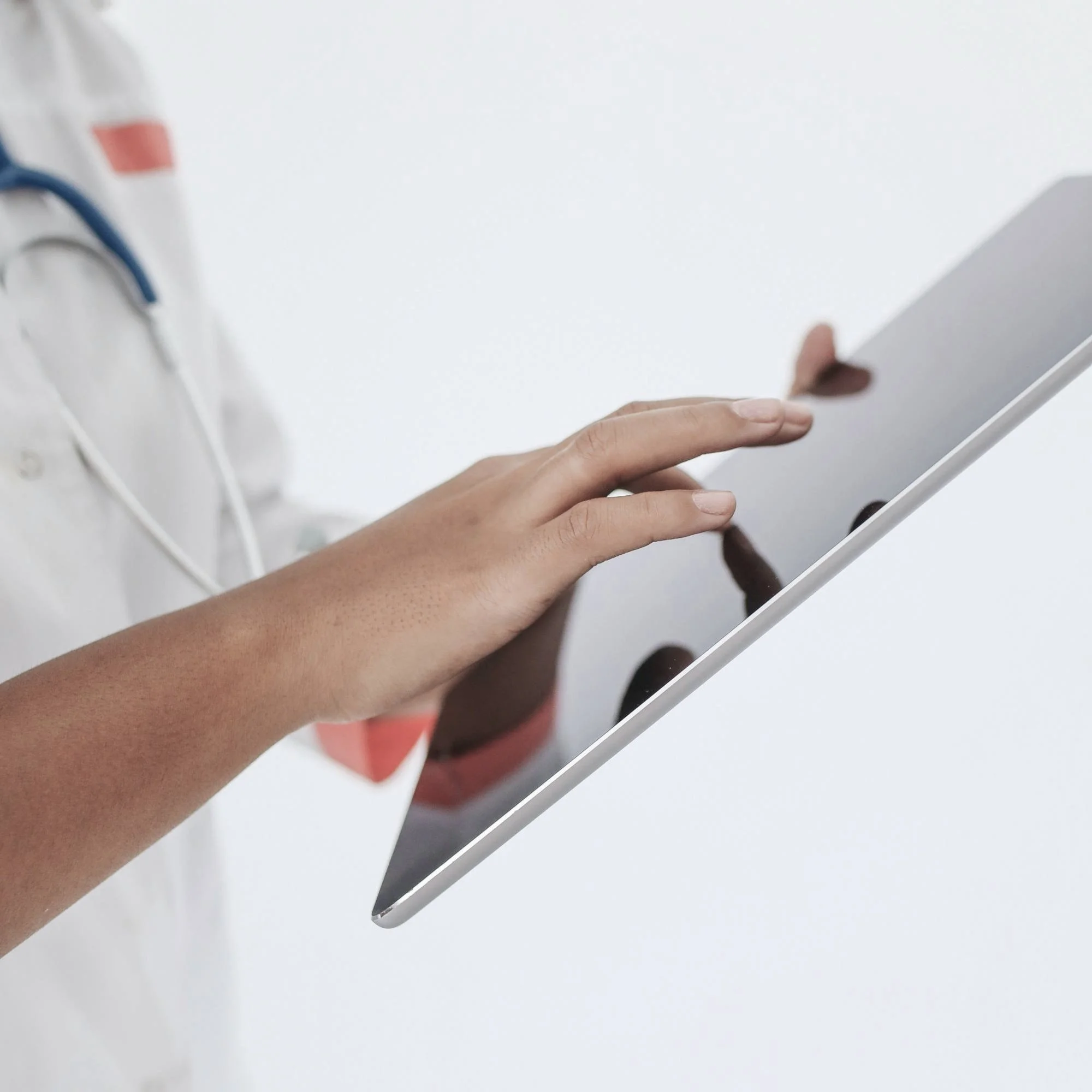 Close-up of a healthcare professional's hand holding a tablet device against a white background.