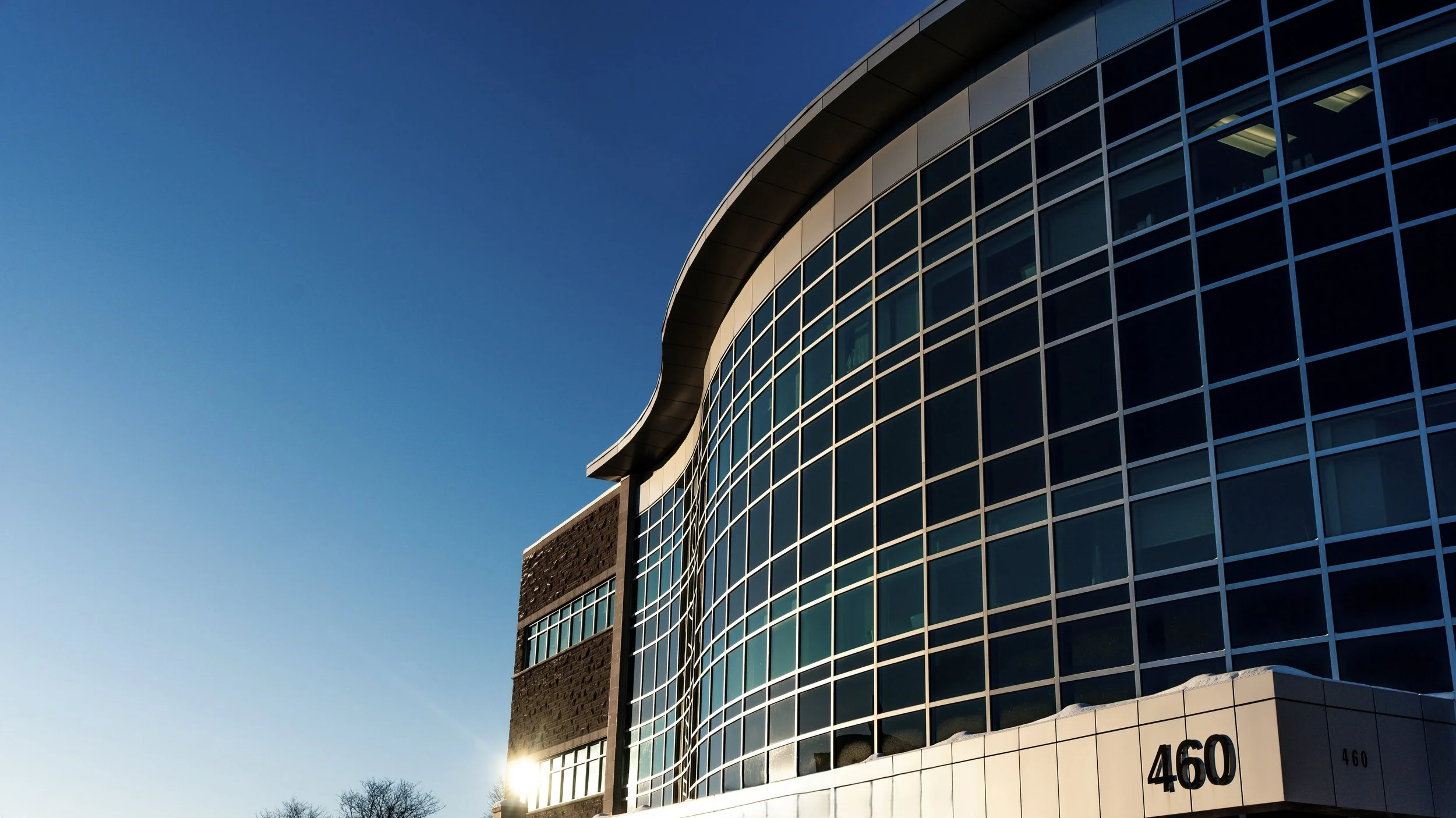 Modern building with curved glass windows at sunset, with the number 460 on the lower corner.