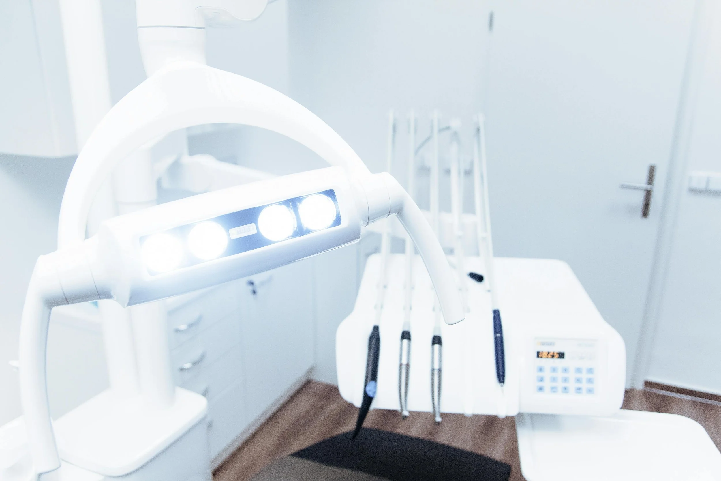Dental examination chair with overhead light, dental tools and a pen on a tray in a white clinic room.