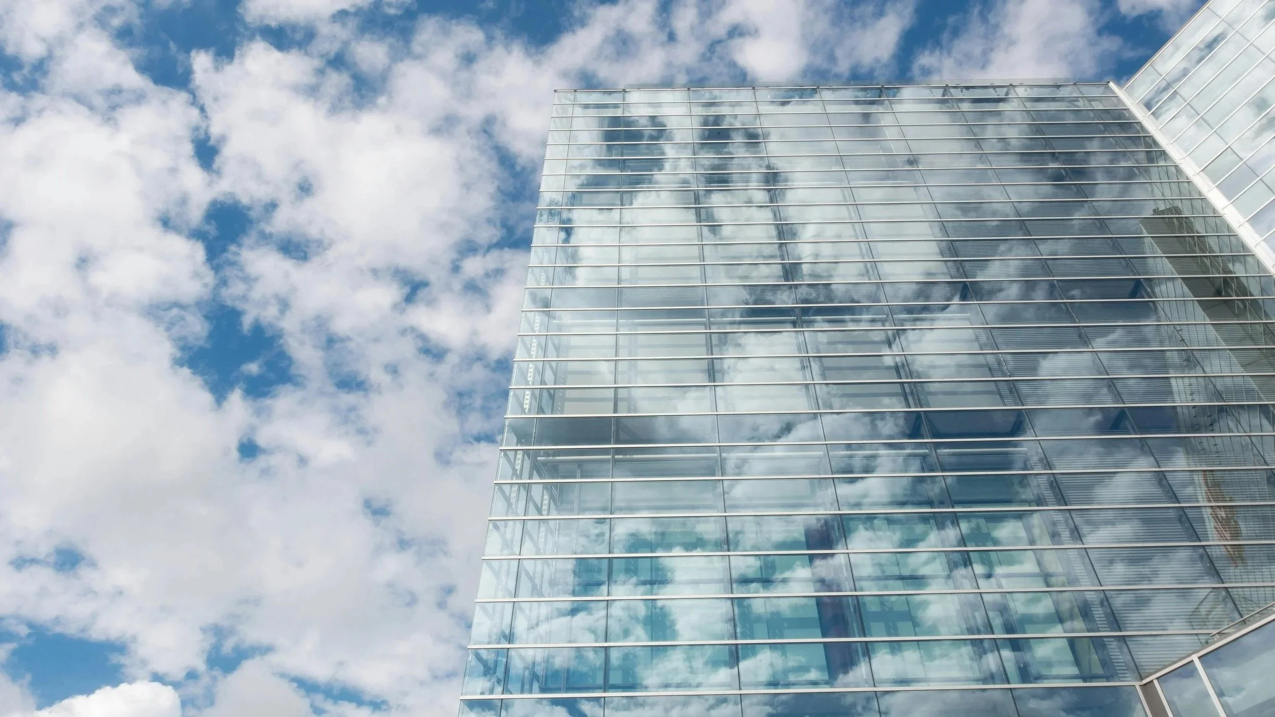 A modern glass skyscraper reflecting the blue sky and white clouds.
