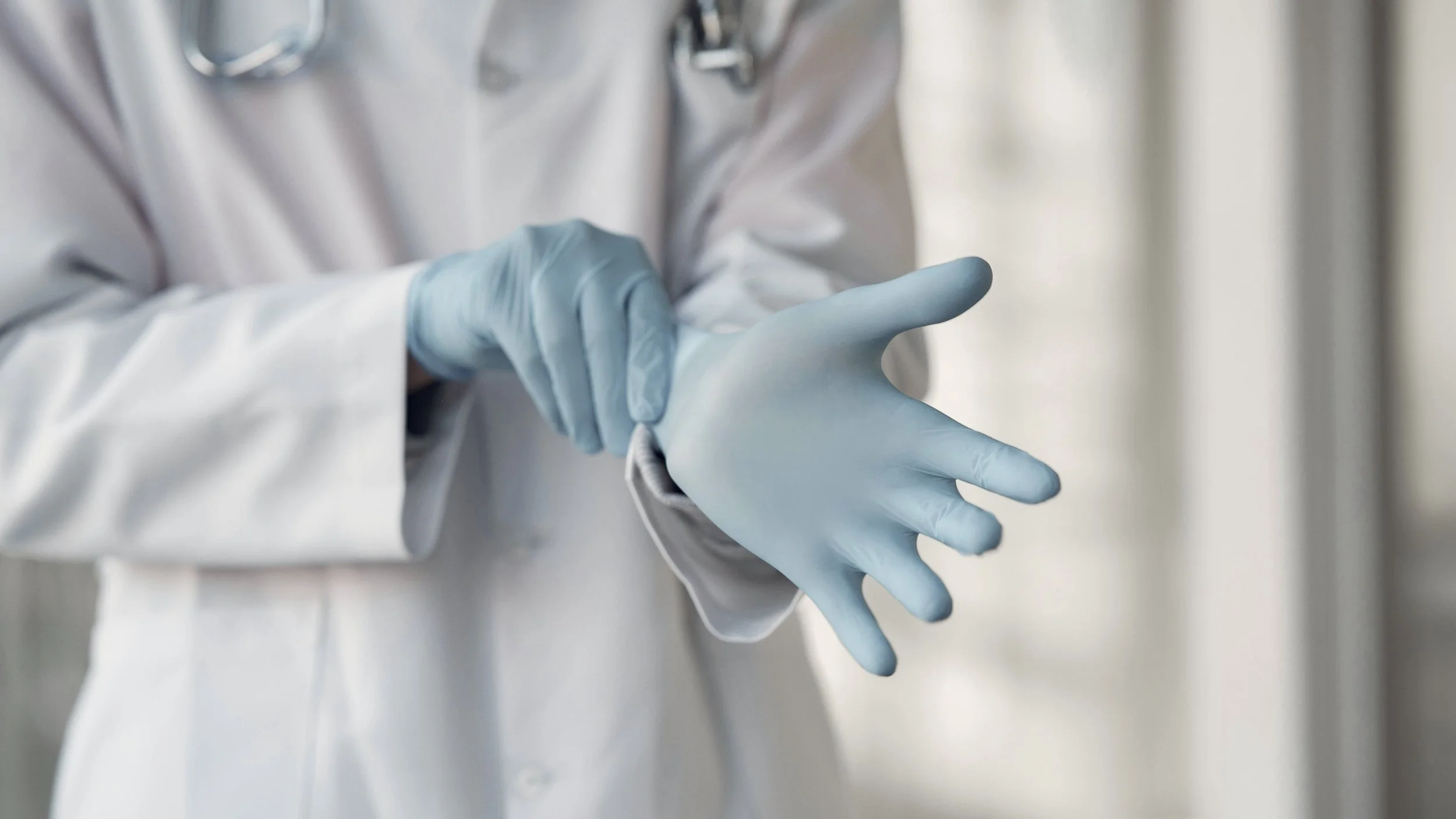 A doctor putting on light blue gloves, with part of a white lab coat visible.