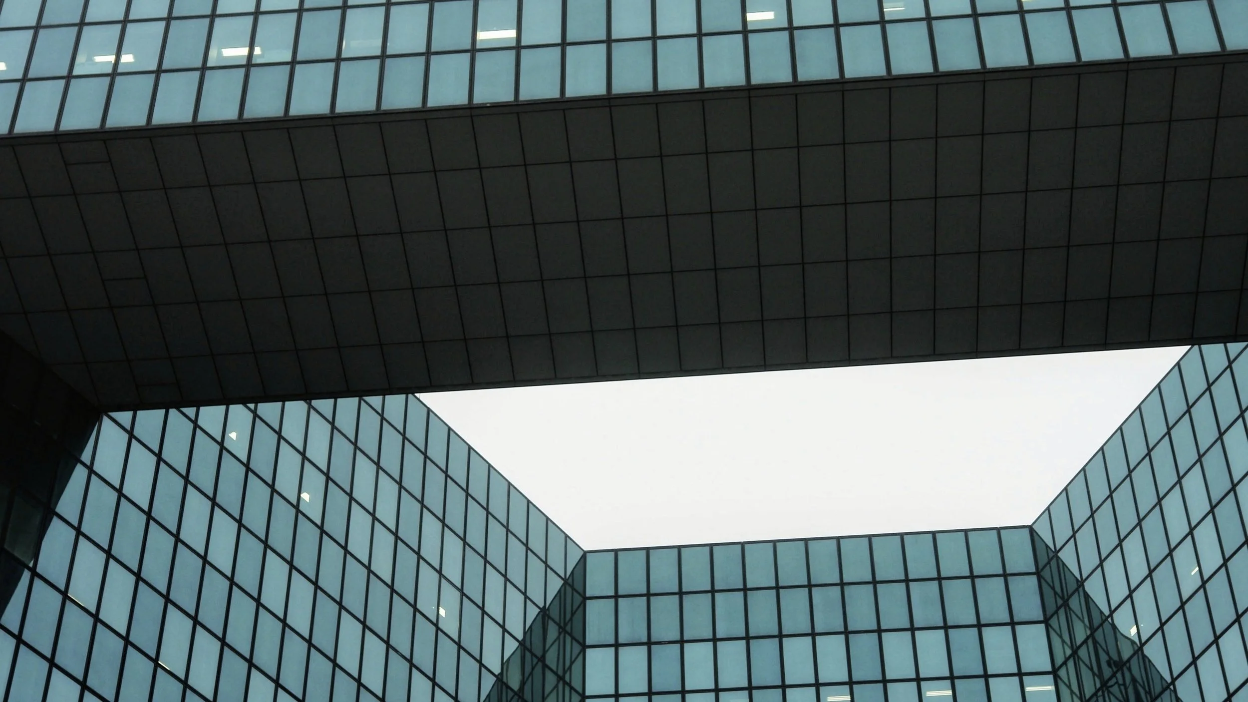Looking up at a modern glass office building with an open sky courtyard in the center, reflecting the sky and surrounding structures.