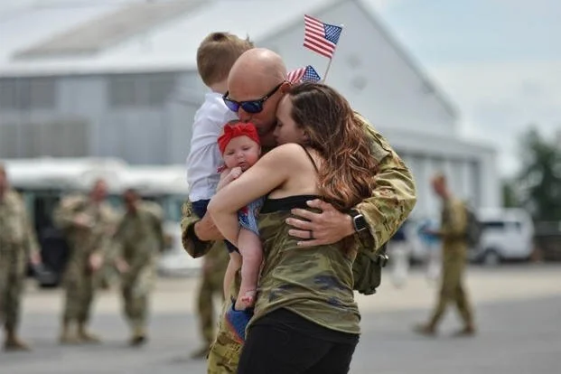 a male veteran hugging a woman and child
