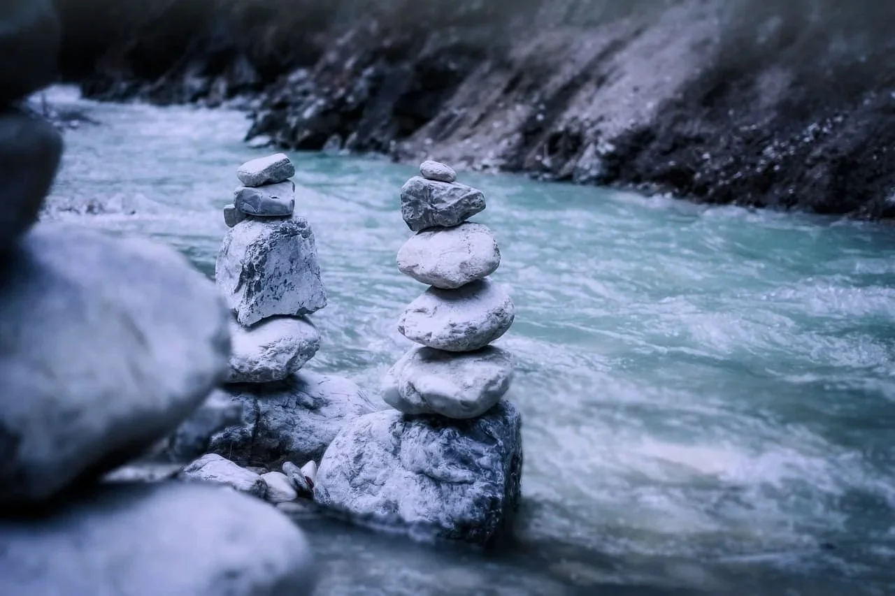 Stacks of balanced stones on the edge of a flowing river in a mountainous area.