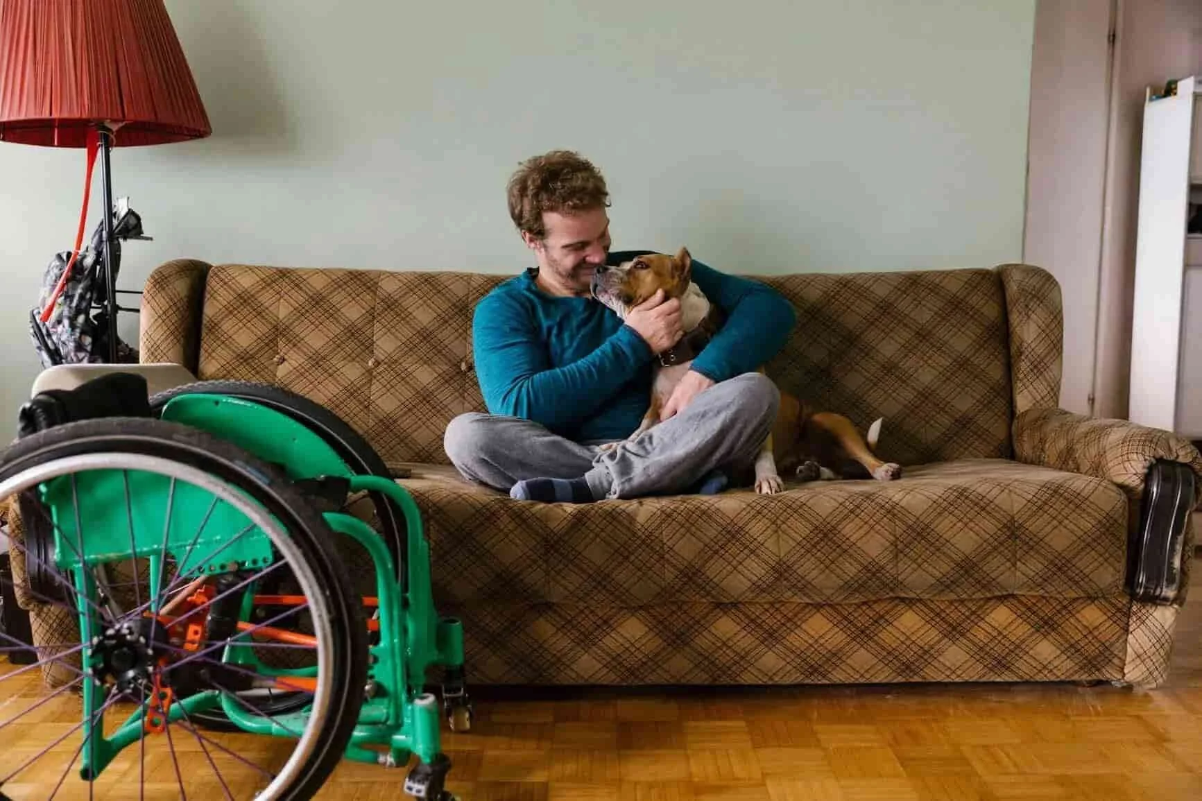 man on couch with small dog. A wheelchair is in front of the couch