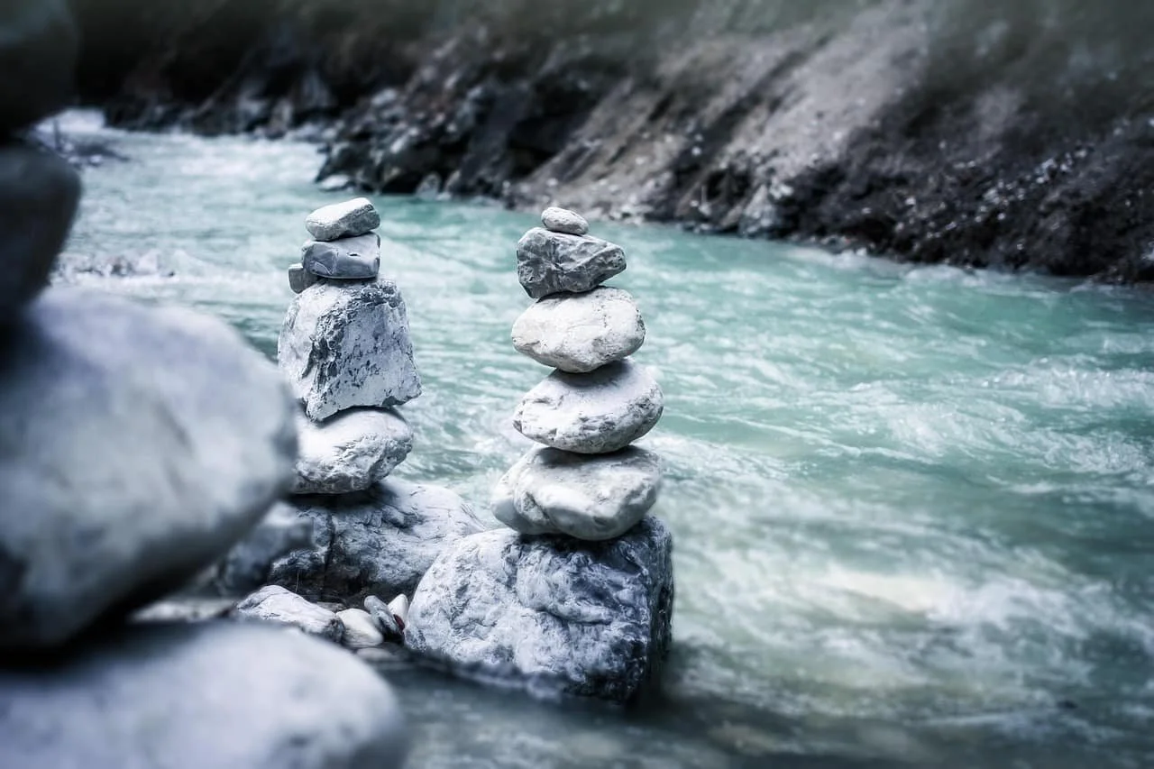 Stacked rocks along a flowing river with rocky cliffs in the background.