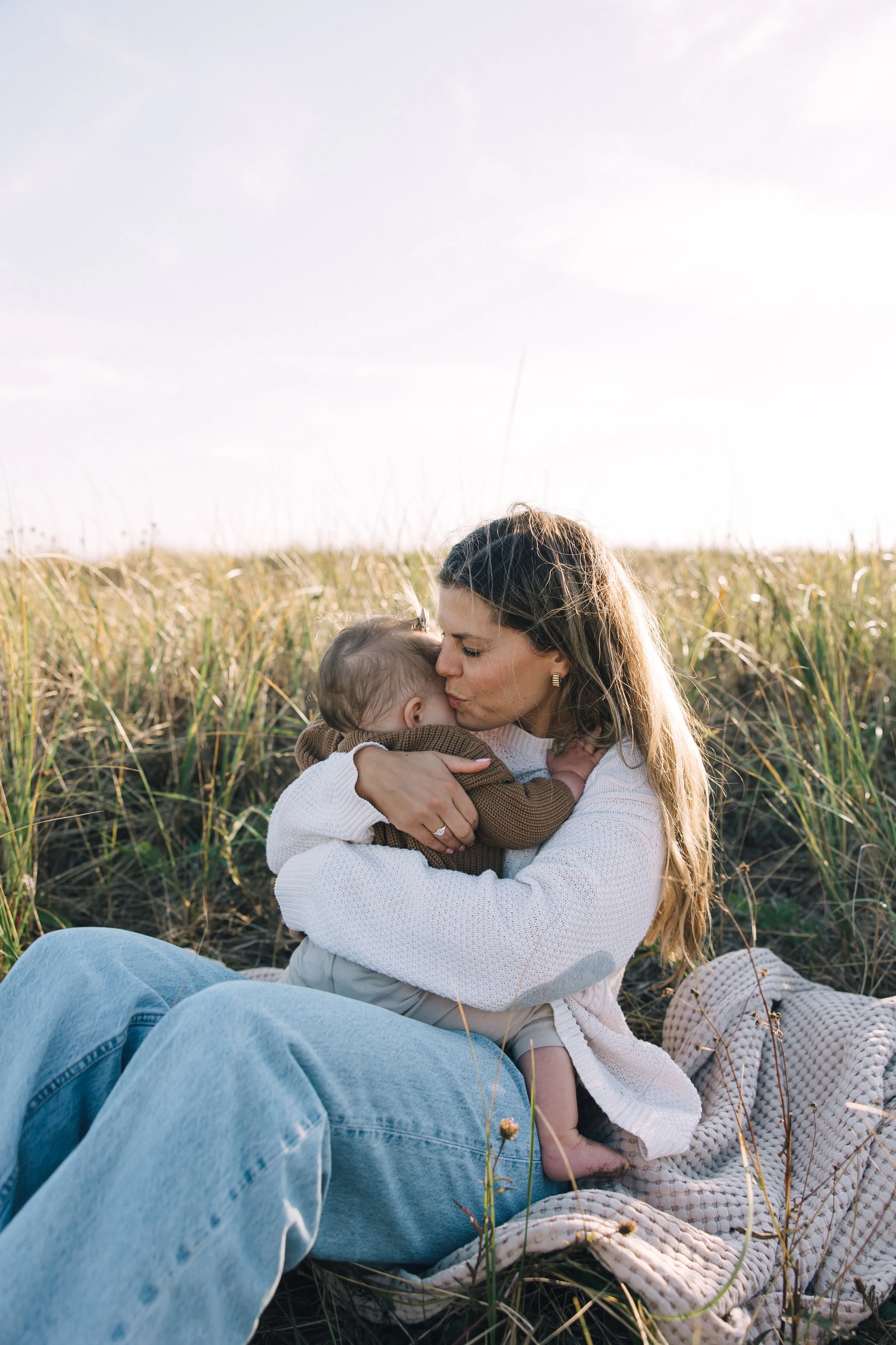 A woman and a child sharing a kiss in a grassy field during sunset.