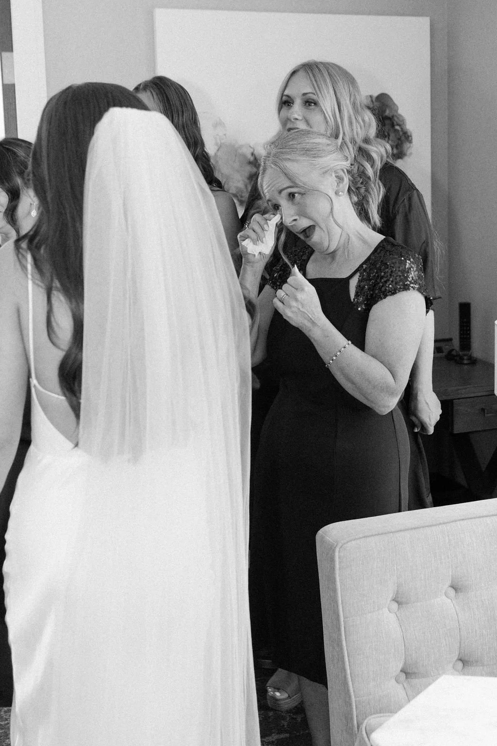 An emotional woman at a wedding, crying and wiping tears while talking to a bride in a white gown and veil.