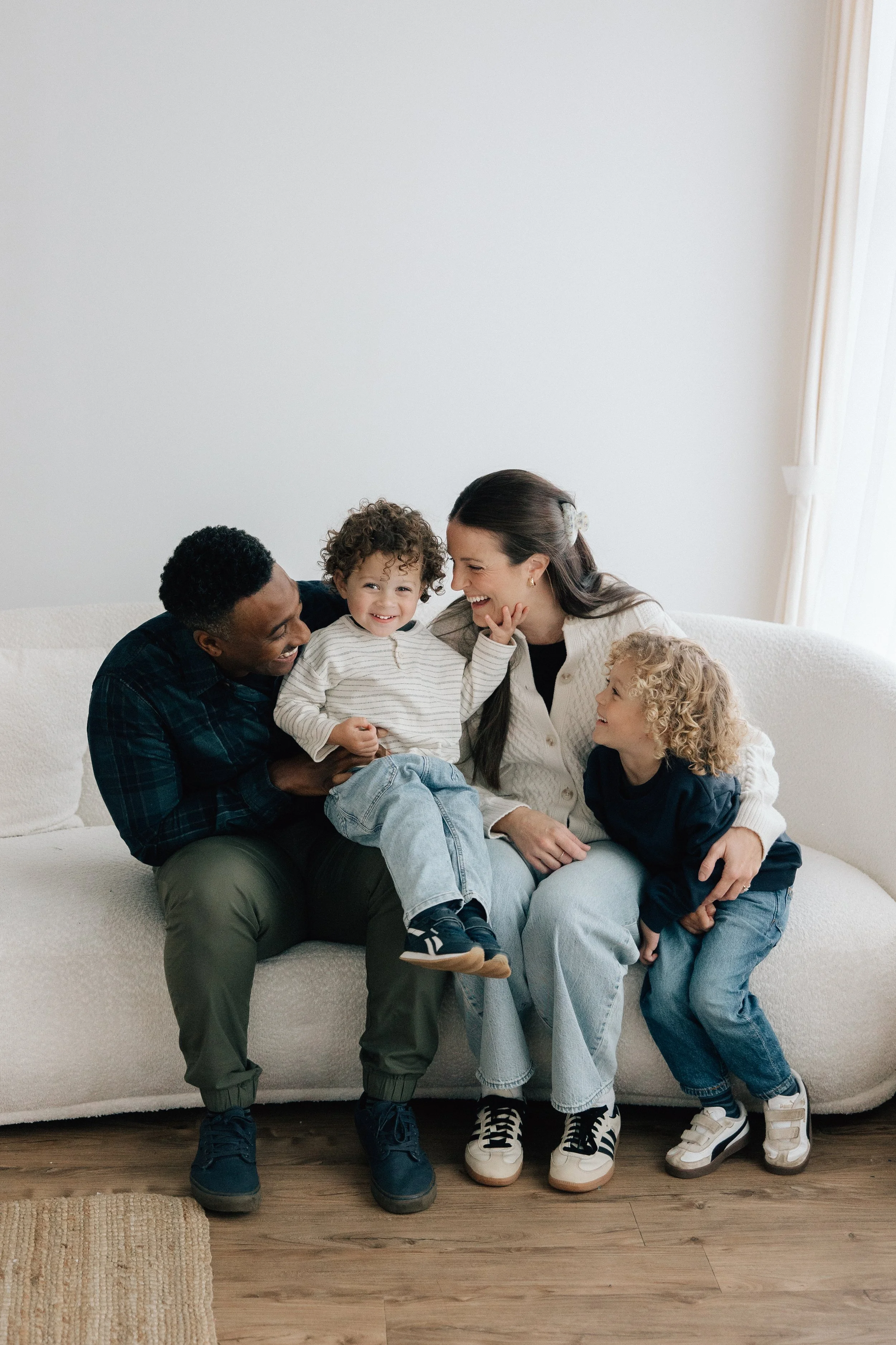 Family of five sitting on a white sofa, smiling and enjoying each other's company in a bright living room.