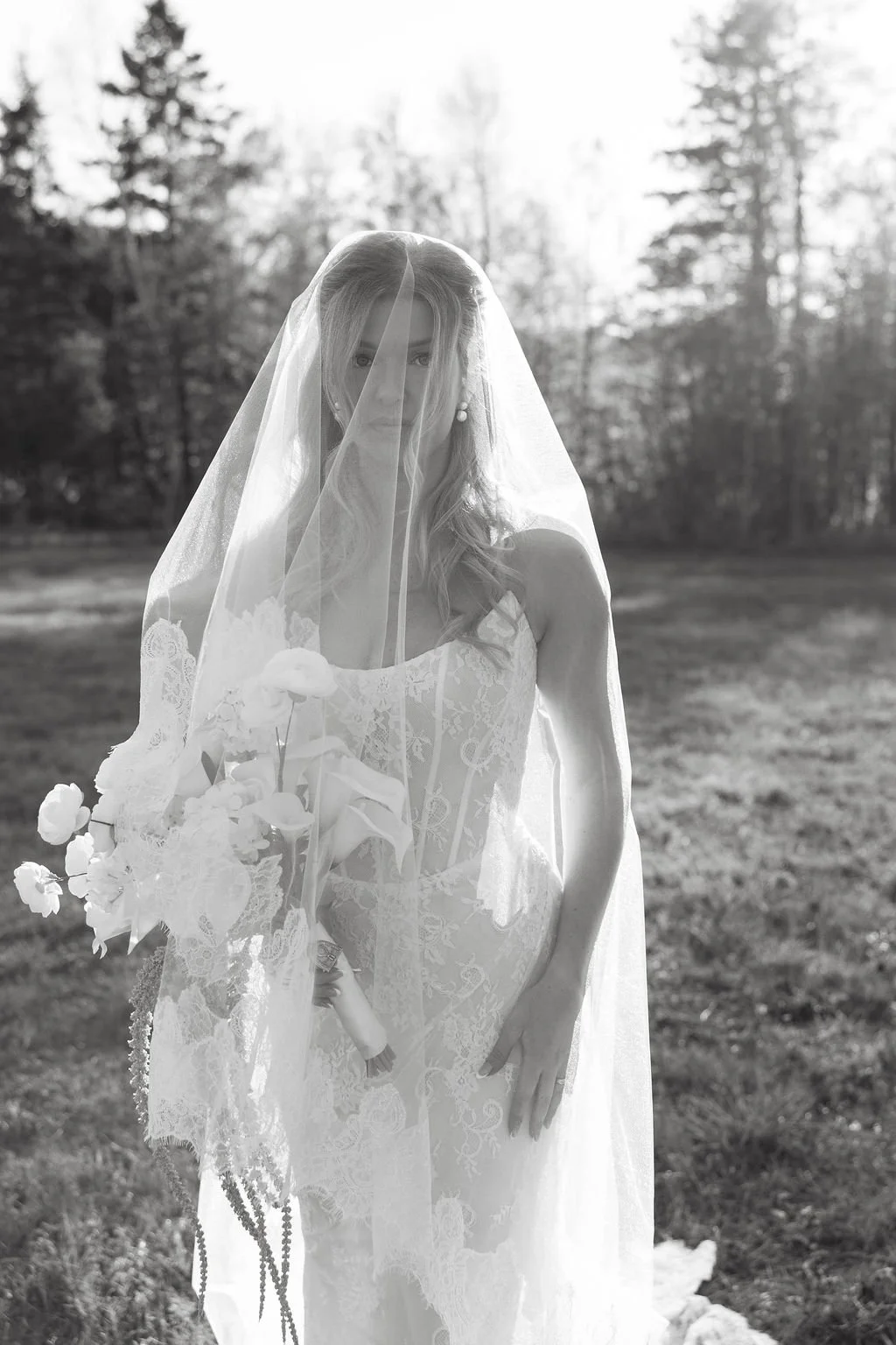A woman in a wedding dress holding a bouquet of flowers outdoors with trees in the background.