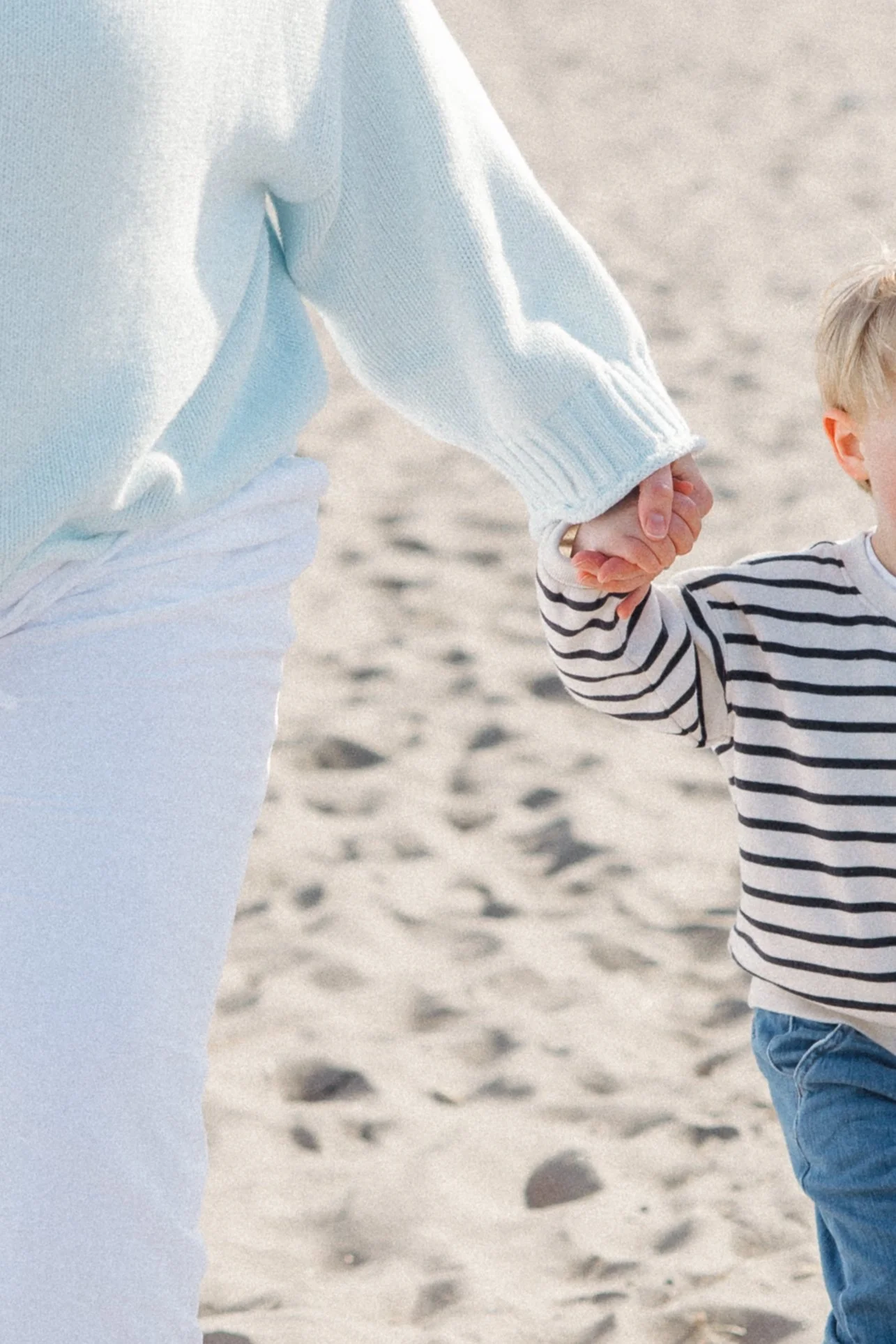 A child walking on the beach holding an adult's hand.