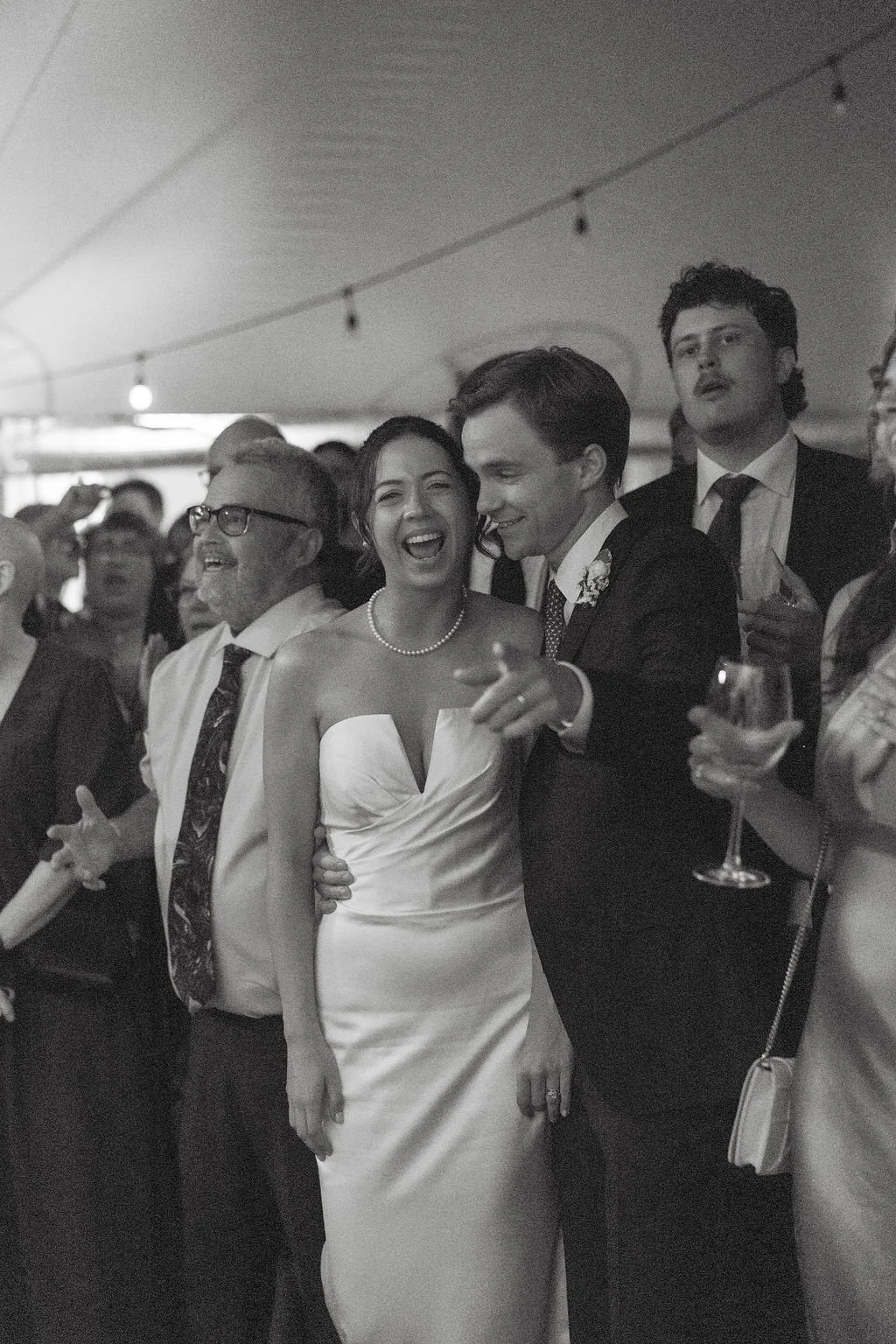 Black and white photo of a wedding reception with a joyful bride and groom dancing and celebrating with guests.