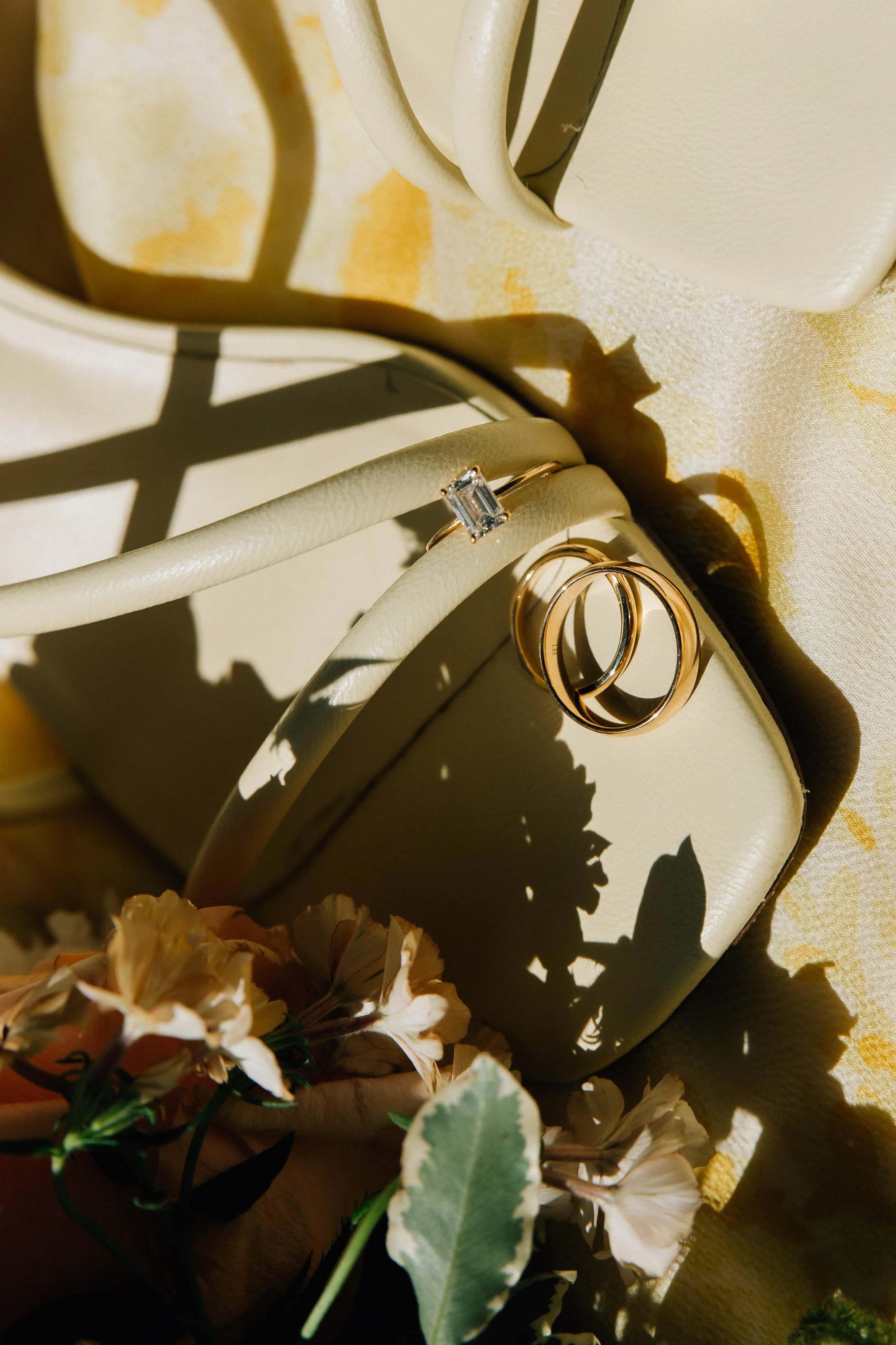 Close-up of gold rings and a ring box on a floral fabric background, with shadows cast by nearby objects.