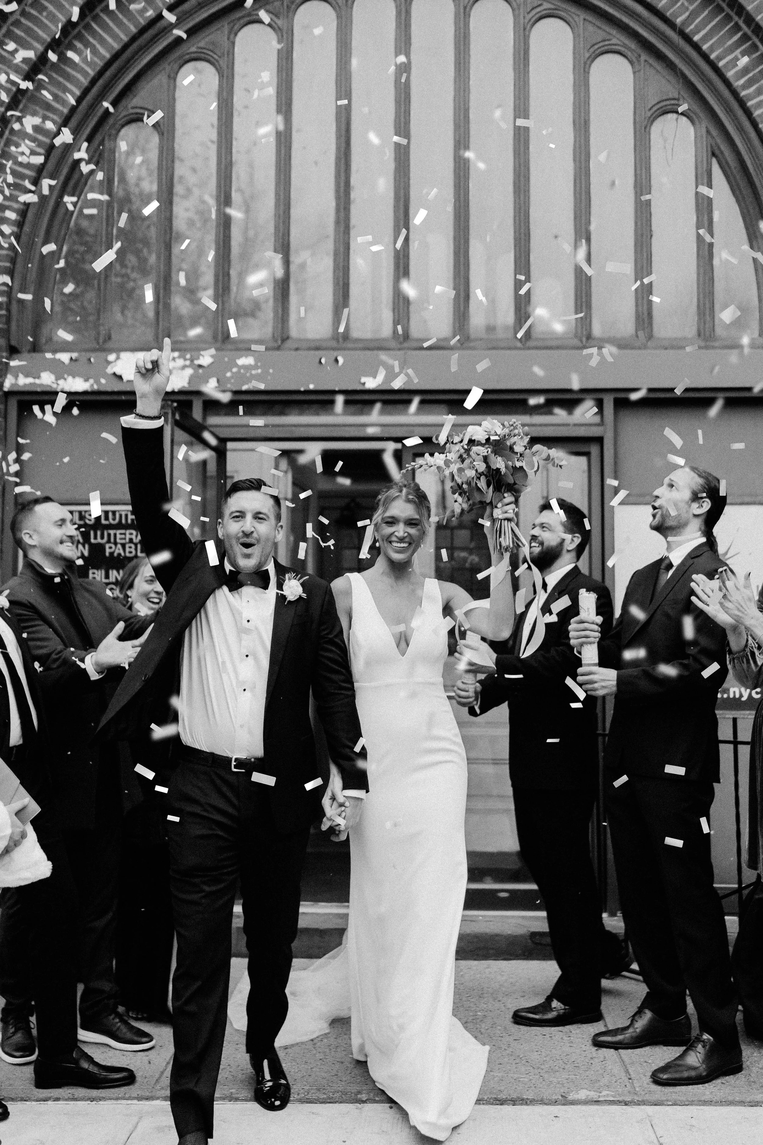 A wedding celebration outside a church with the bride and groom leading, surrounded by friends and family, confetti falling, and everyone smiling and cheering.