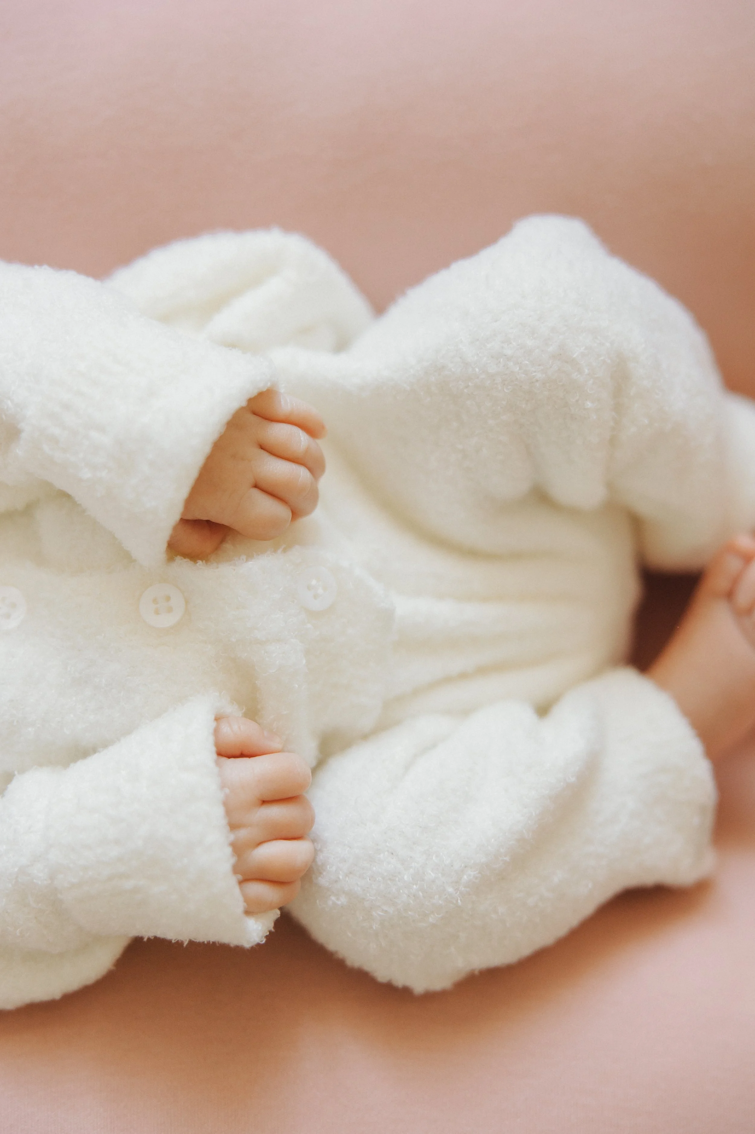 Close-up of a newborn baby's hand grasping the side of a soft, white blanket, with the baby's face not visible.