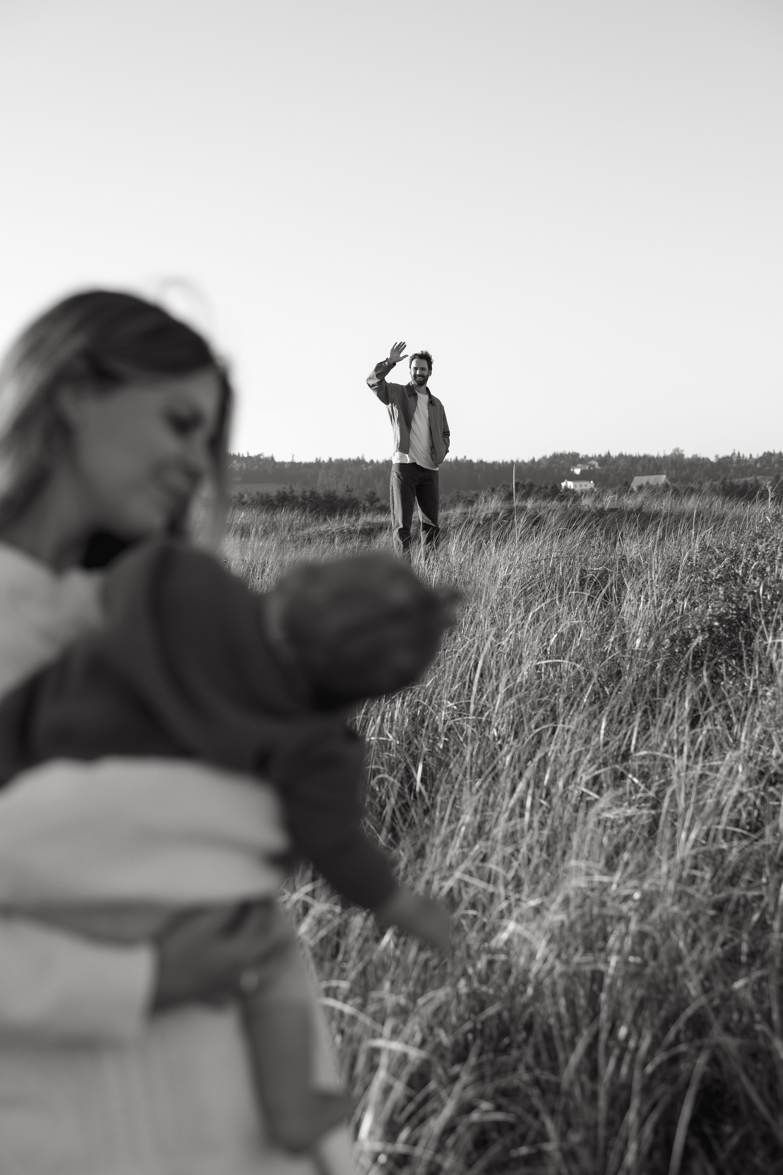 A man standing in a field and waving, with a woman in the foreground out of focus.