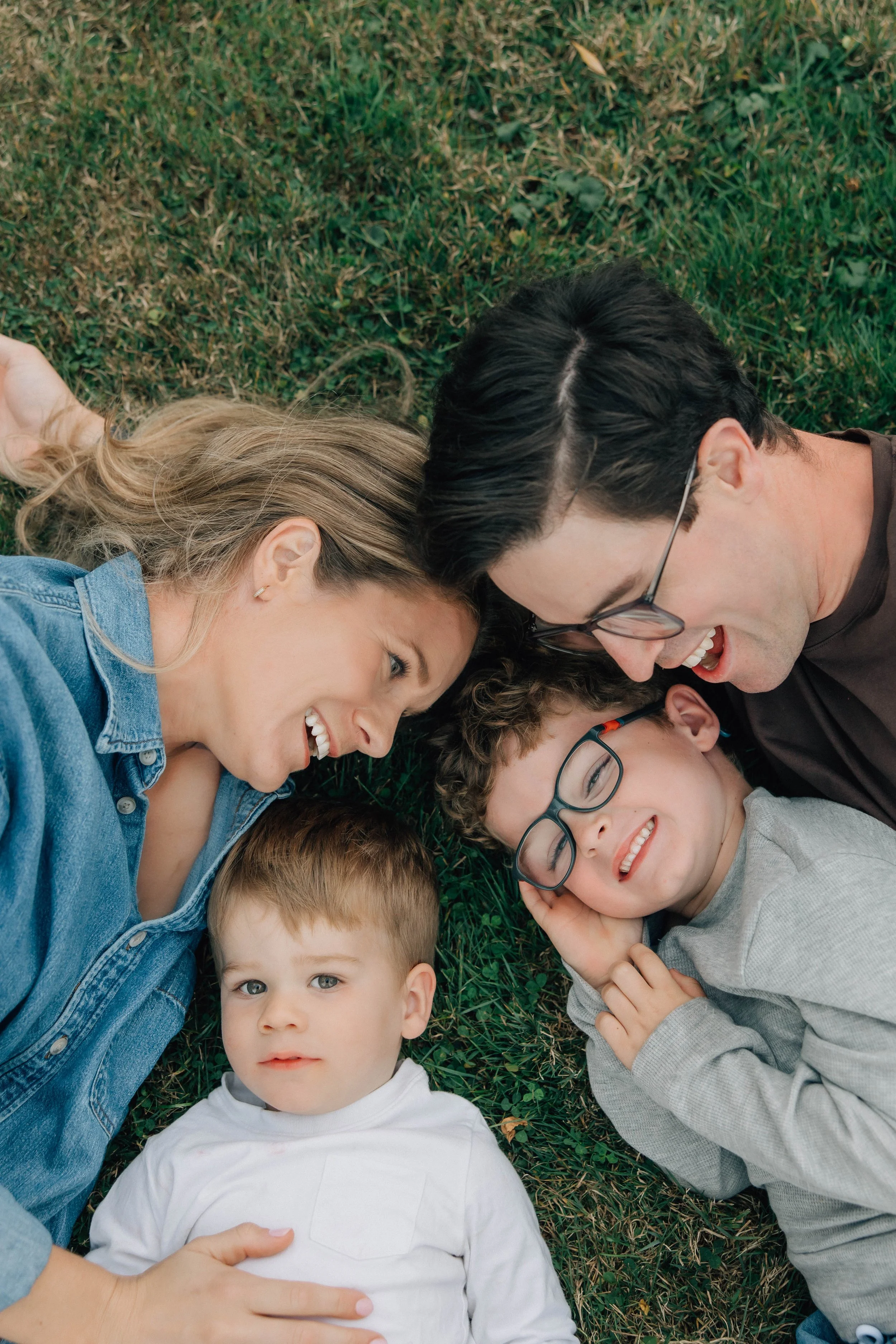 Family of six lying on grass, smiling and looking at the camera, with their heads close together.
