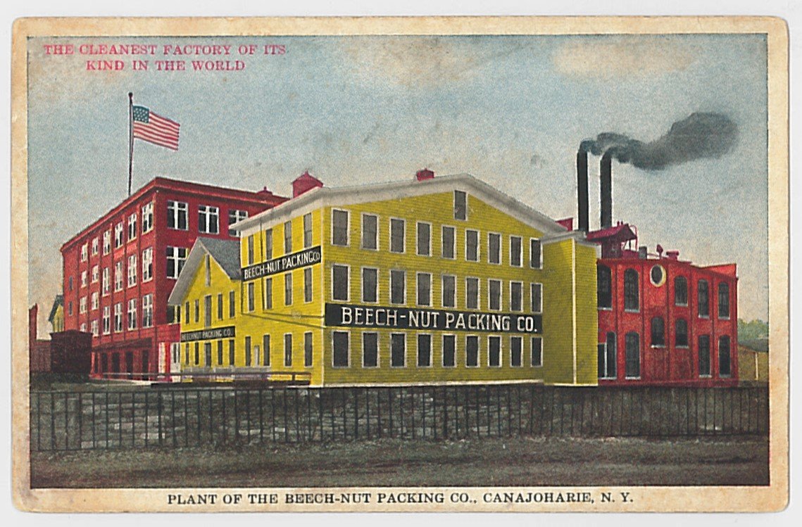 Color photo post card showing yellow and red factory buildings. The yellow building has a sign that reads: Beech-Nut Packing Co. 