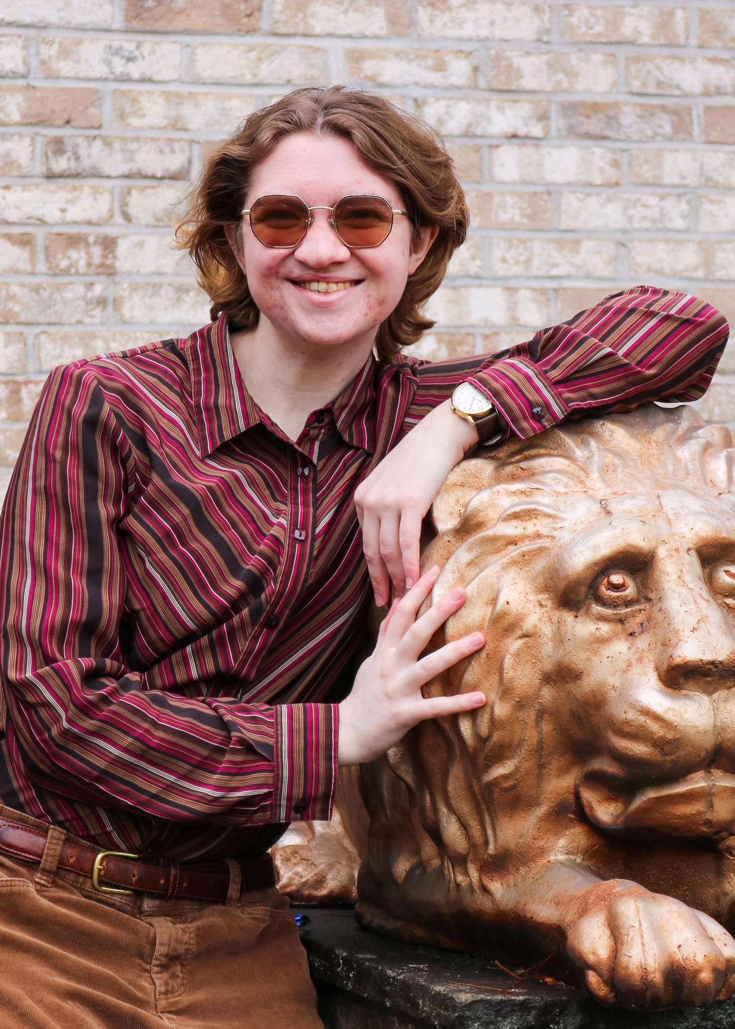 Woman in a plaid long sleeve shirt leaning on a statue of a lion. She wears sunglasses and is smiling