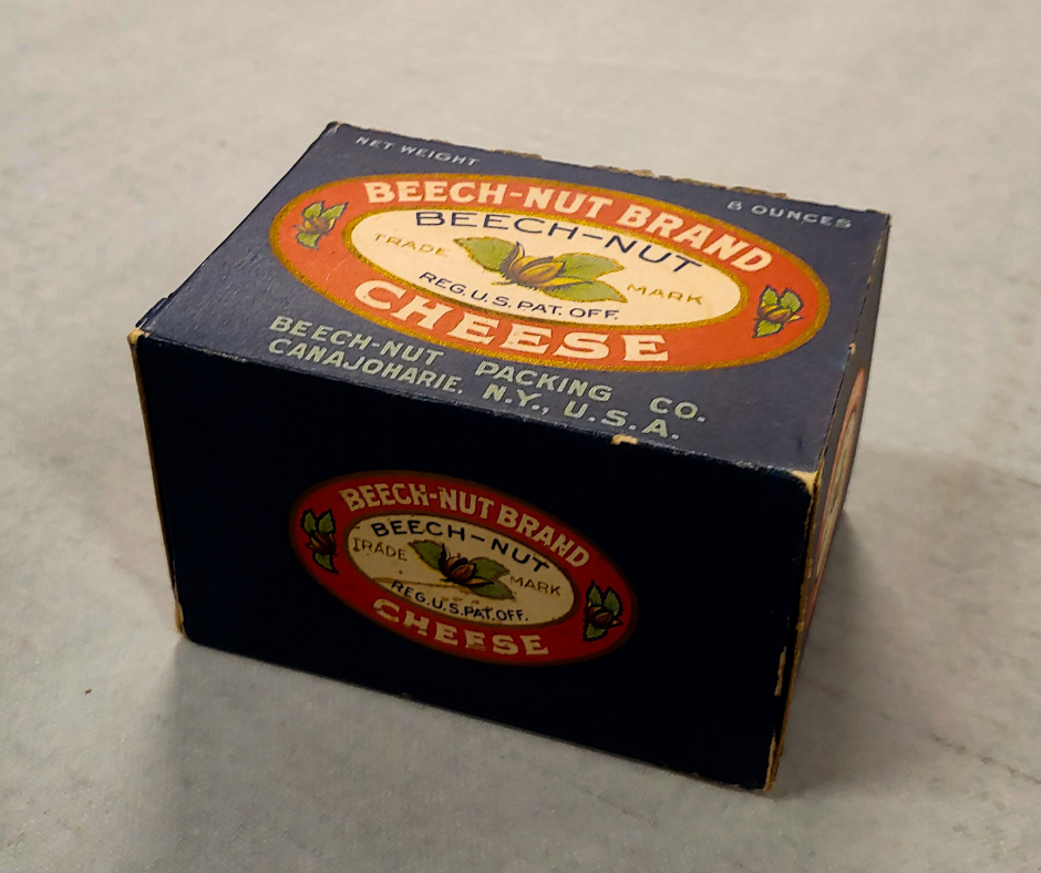  a rectangular blue box with the Beech-Nut company logo on top and sides. The logo is a red circle with a cream center. The red circle reads: Beech Nut Brand Cheese. Inside the cream circle it reads Beech-Nut with an illustration of a beech nut with 