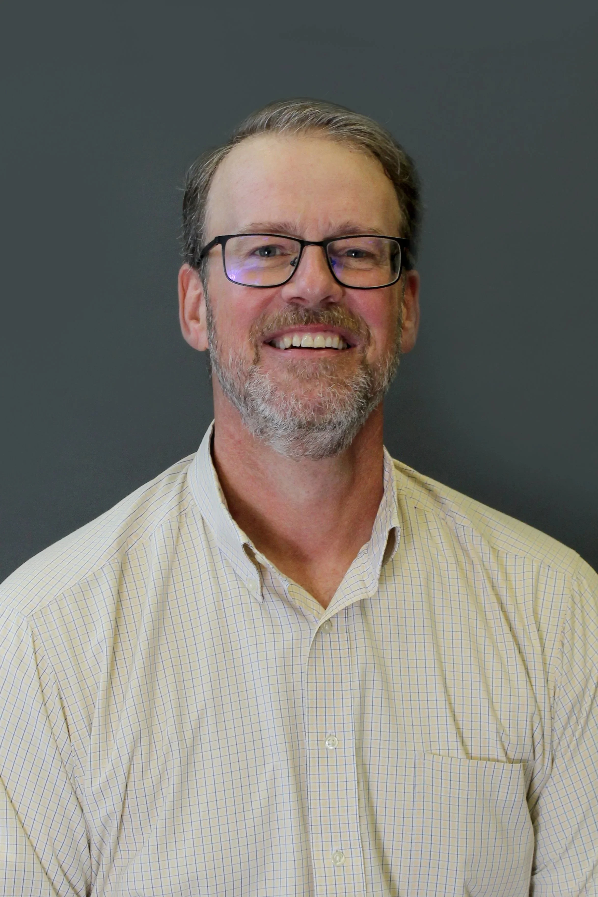 This is a photo of trustee Andrew LaCoppola. He is wearing an off-white collared shirt and black glasses.