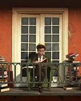 Man sitting on a balcony reading a book. There are stacks of books on either side of him. 