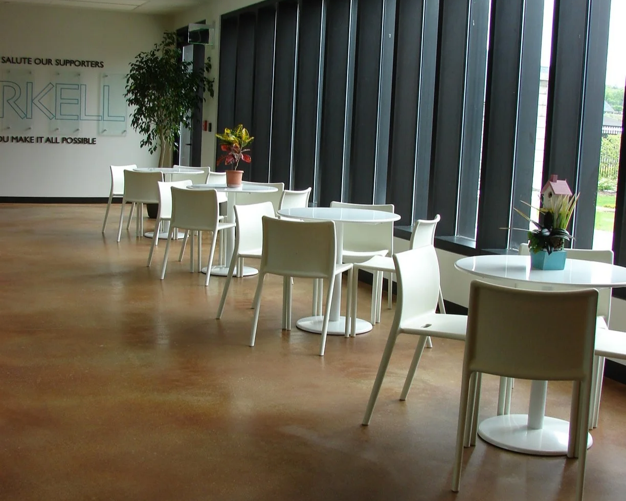 This is an image of the Cafe area at the Arkell Museum and Canajoharie Library. There are four white small round tables accompanied by four white armless chairs at each. They are staged with small floral centerpieces.