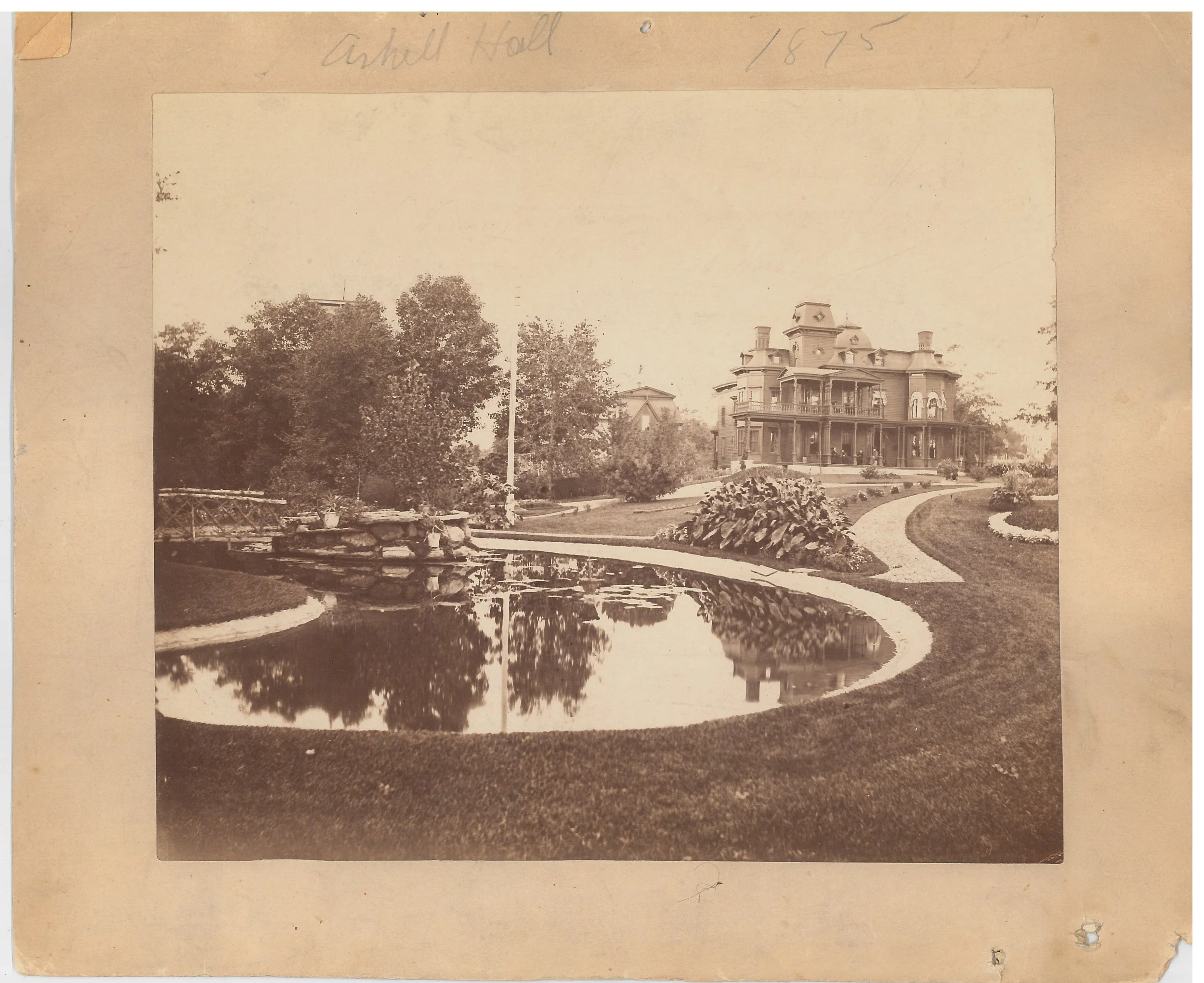Black and white photo of a large house with a pond in the foreground