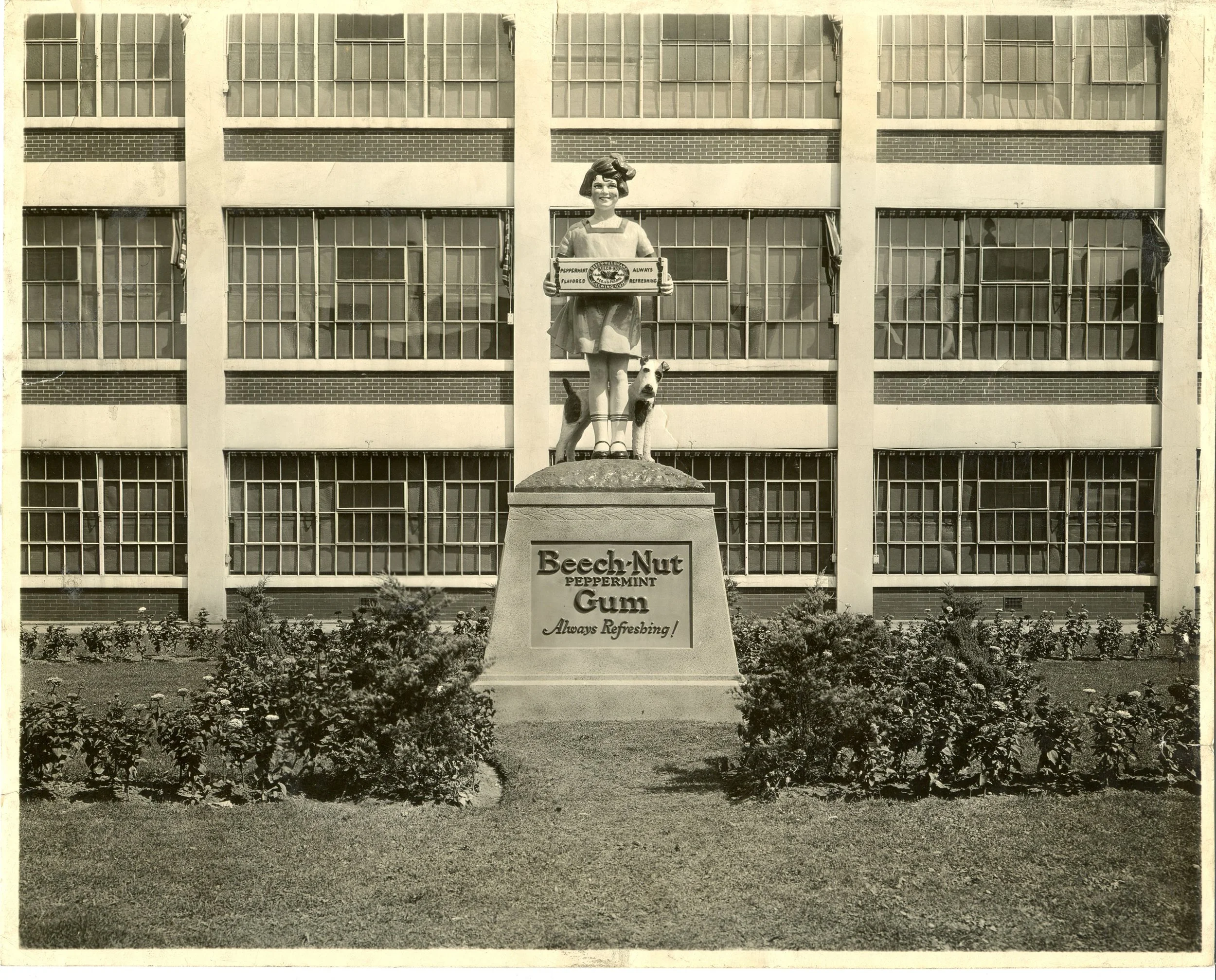 Black and white photo of a statue of a girl and a dog in front of a large building with many windows.
