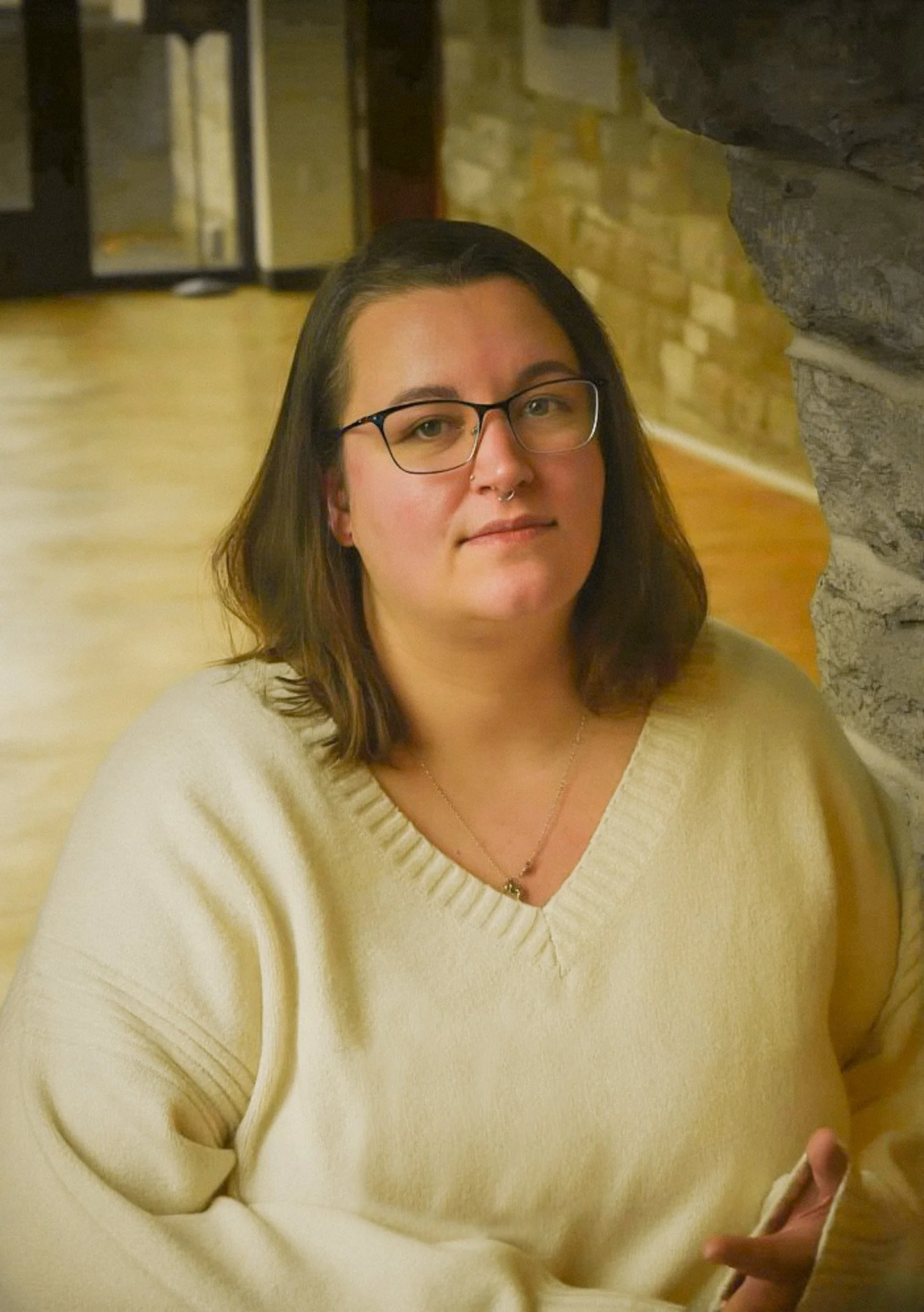 Photo of a woman in a white shirt looking at the camera. She has shoulder length hair and wears glasses.
