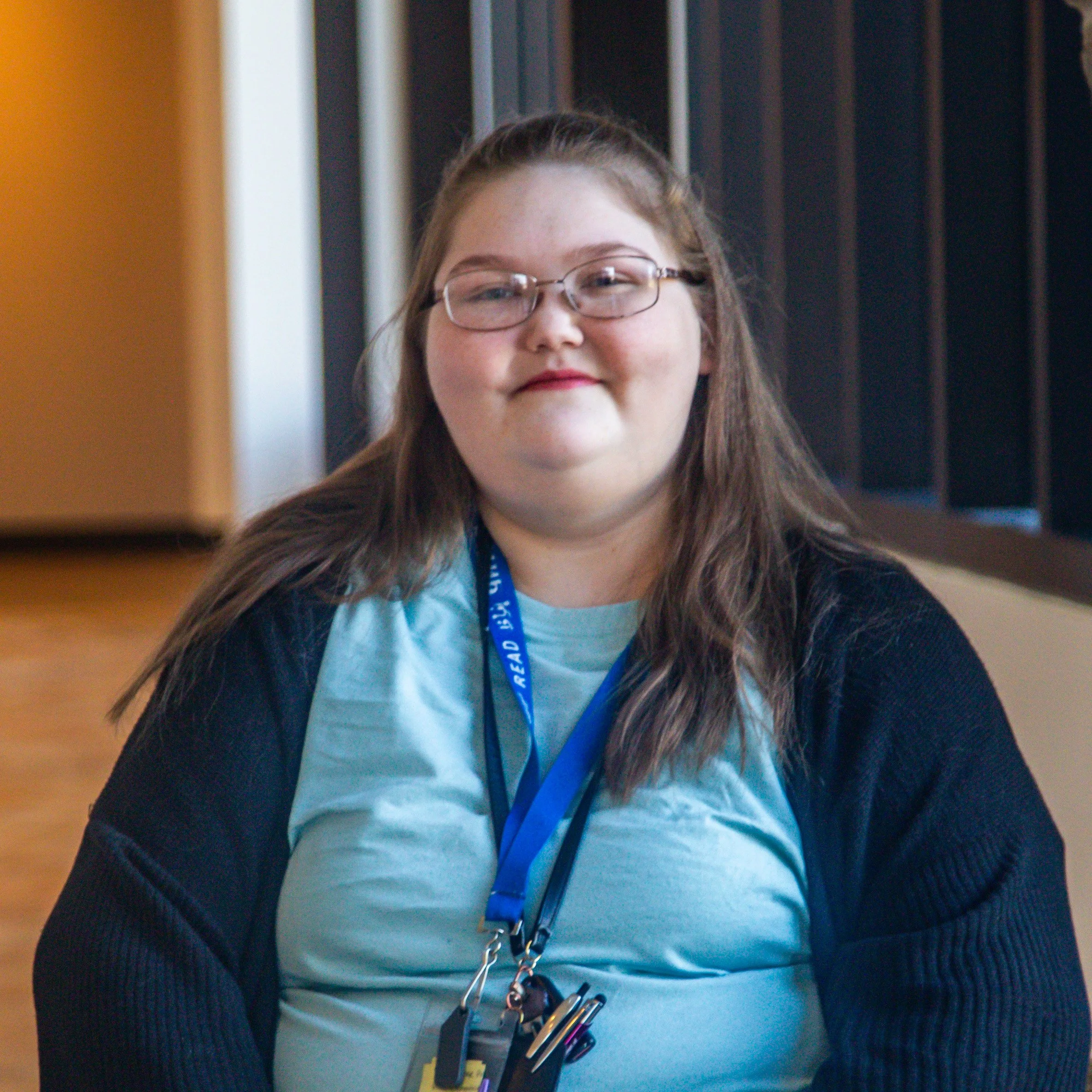 Woman with long light brown hair wearing a blue shirt and a black cardigan. She wears glasses with thin frames