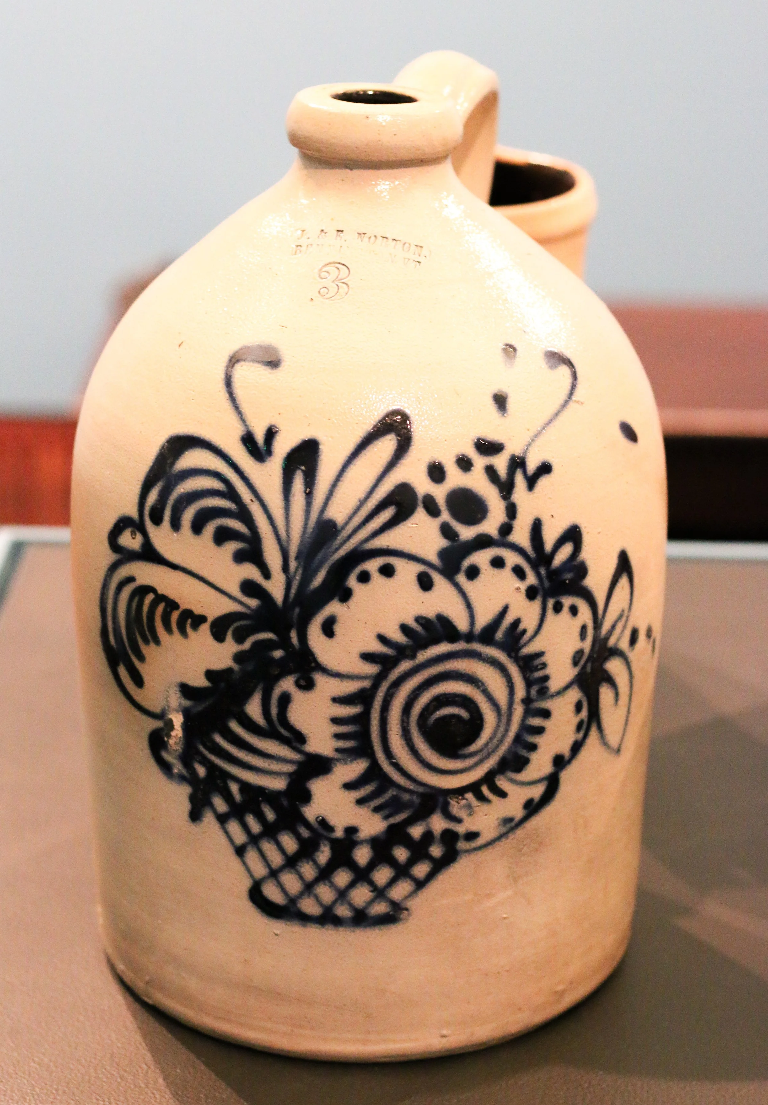 Salt glazed stoneware jug with blue flowers painted on the front of it.
