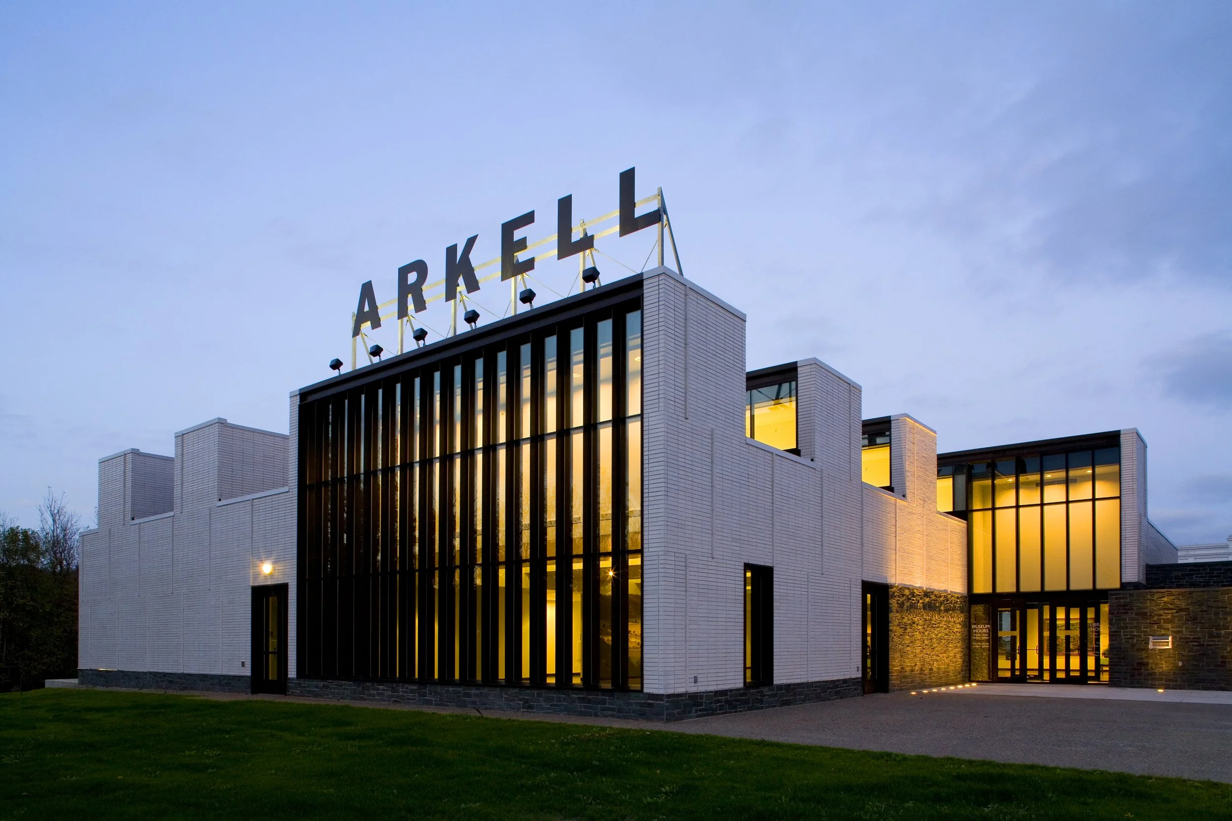 Picture of a large white building with vertical windows and a sign on the roof that says Arkell
