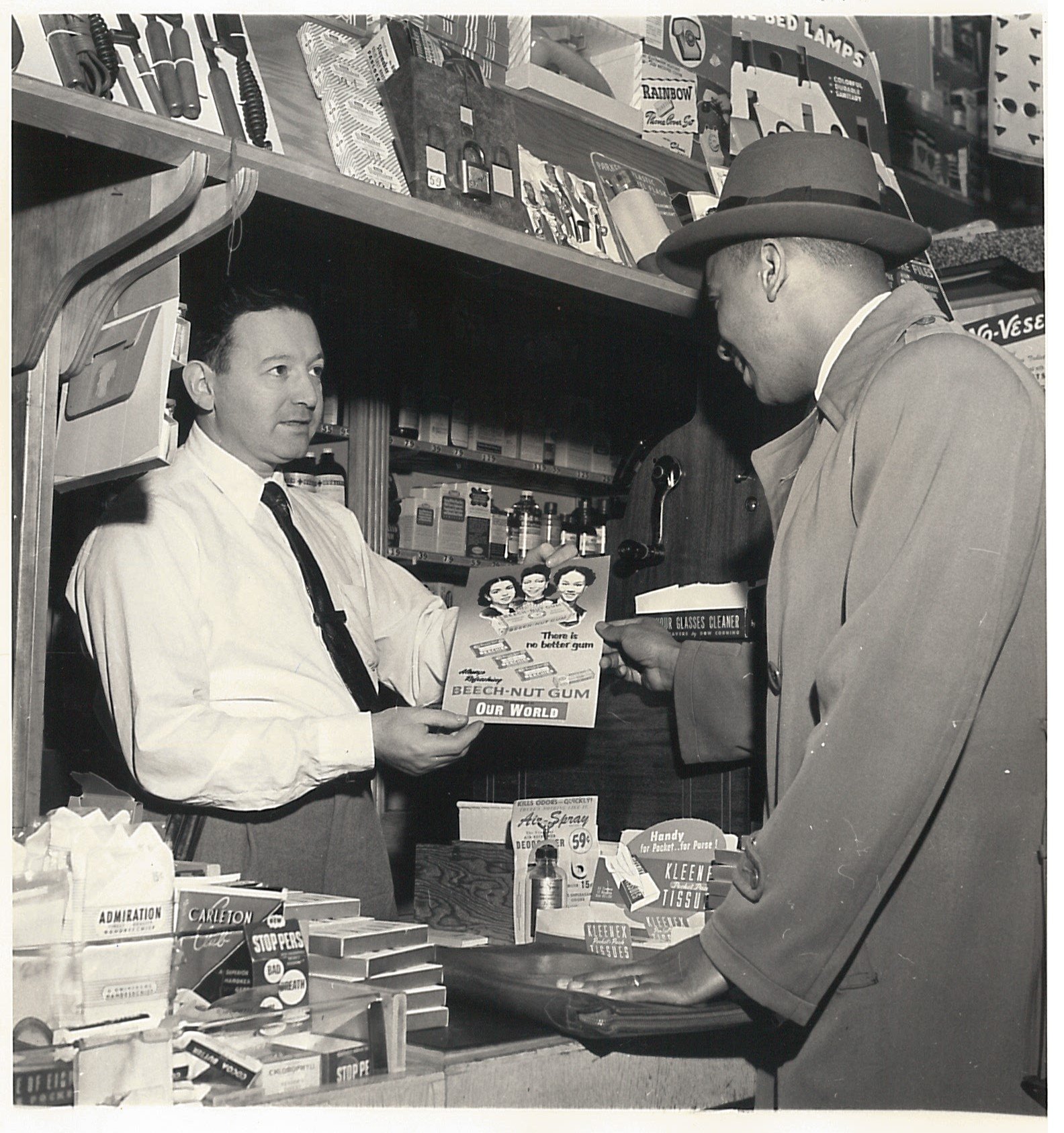 Black and white photograph of two men talking to one another as they look at a Beech-Nut advertisement.