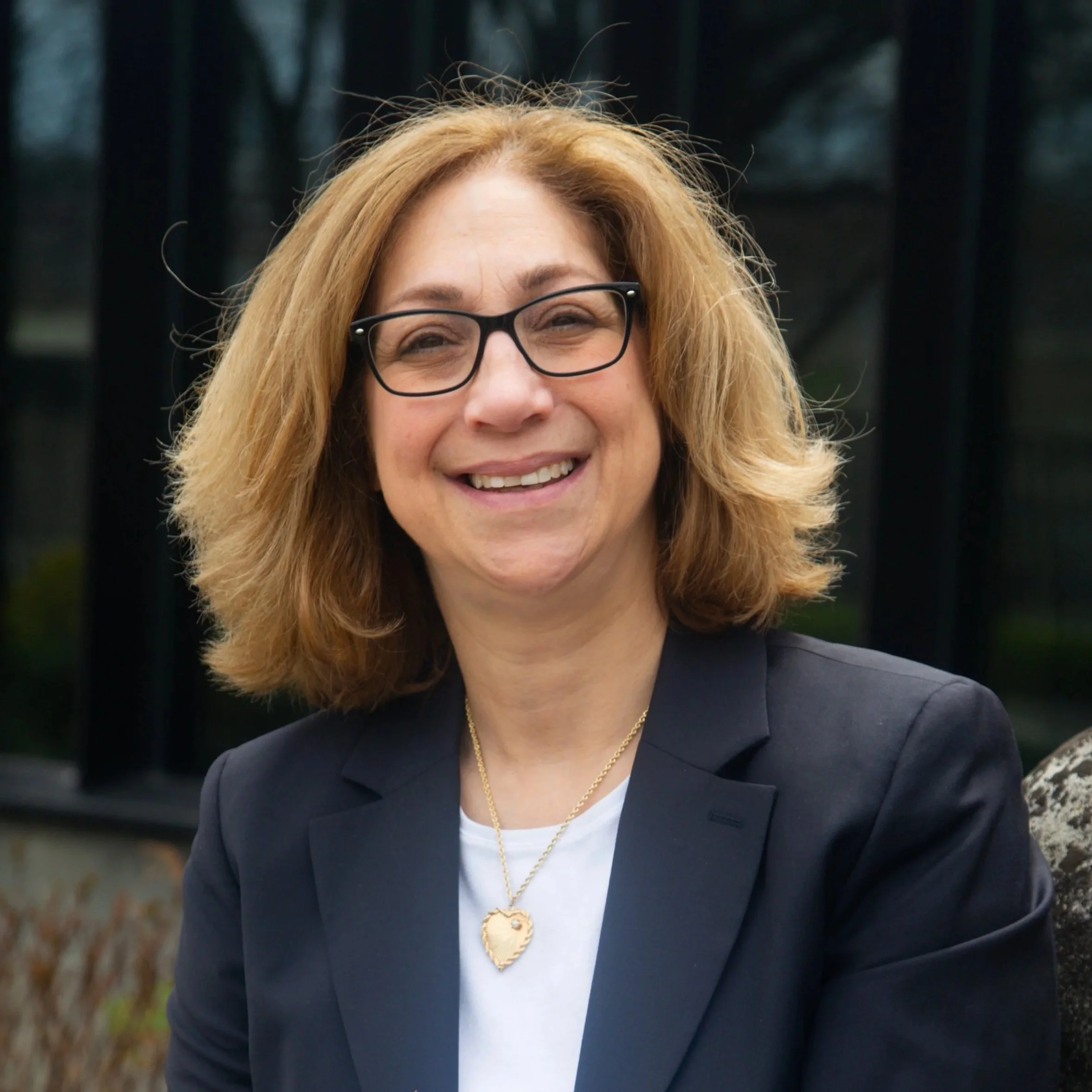 Photo of a woman with shoulder length brown hair. She looks at the camera and smiles. She is wearing a dark blazer and a white shirt.