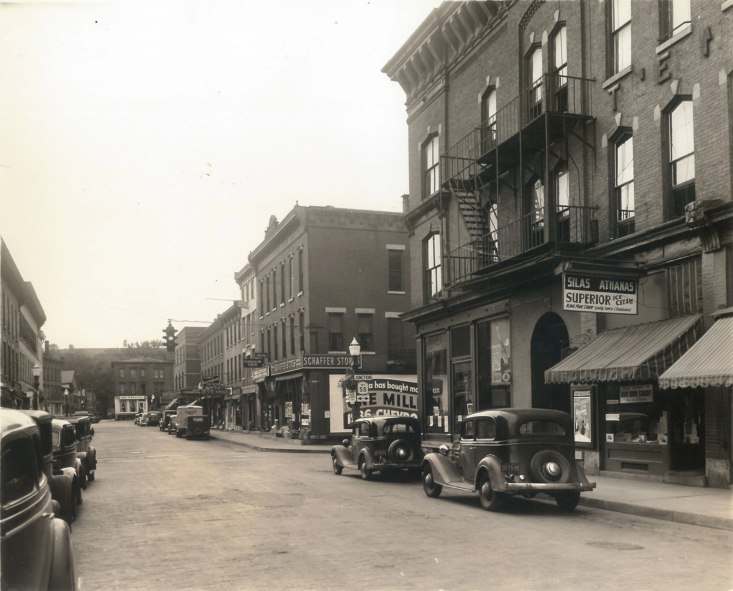 Black and white photo of a downtown area with brick buildings and cars from the 1930s